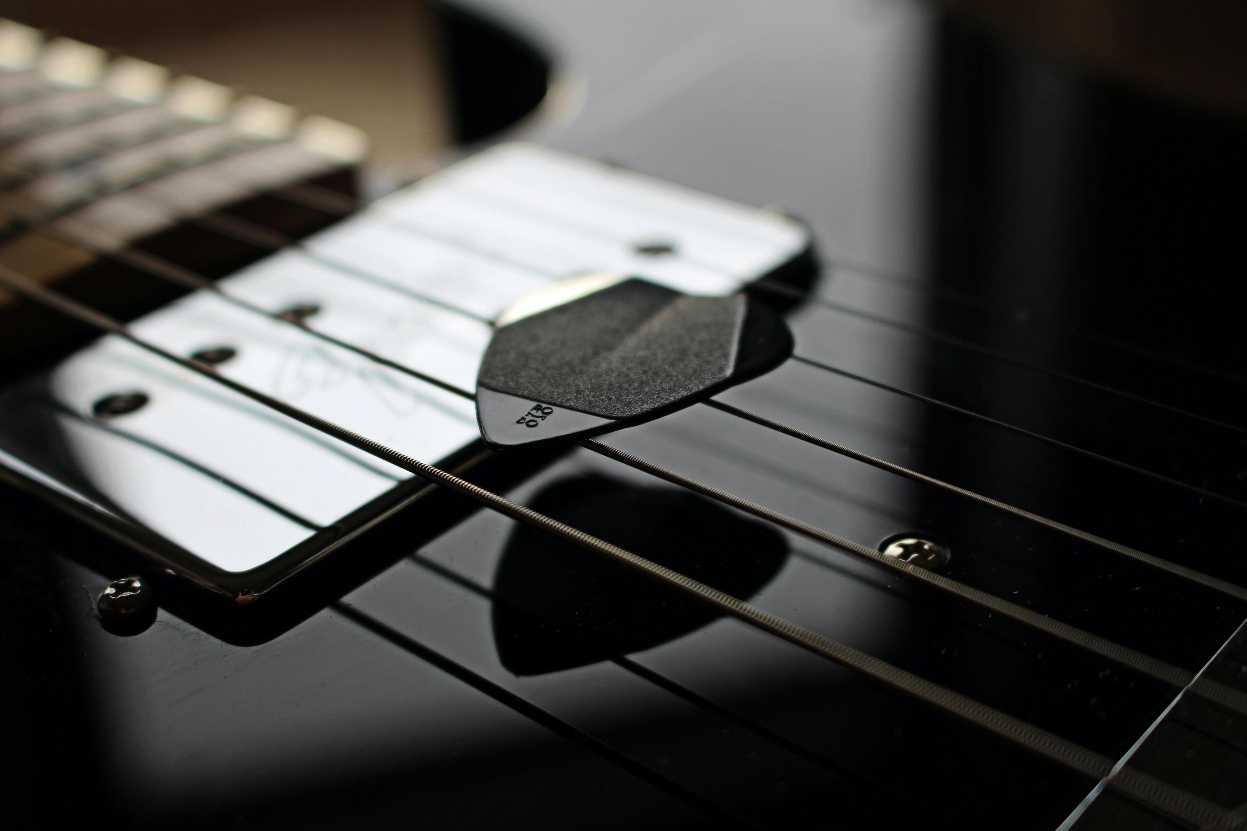 Et plekter hviler på gitarstrenger.