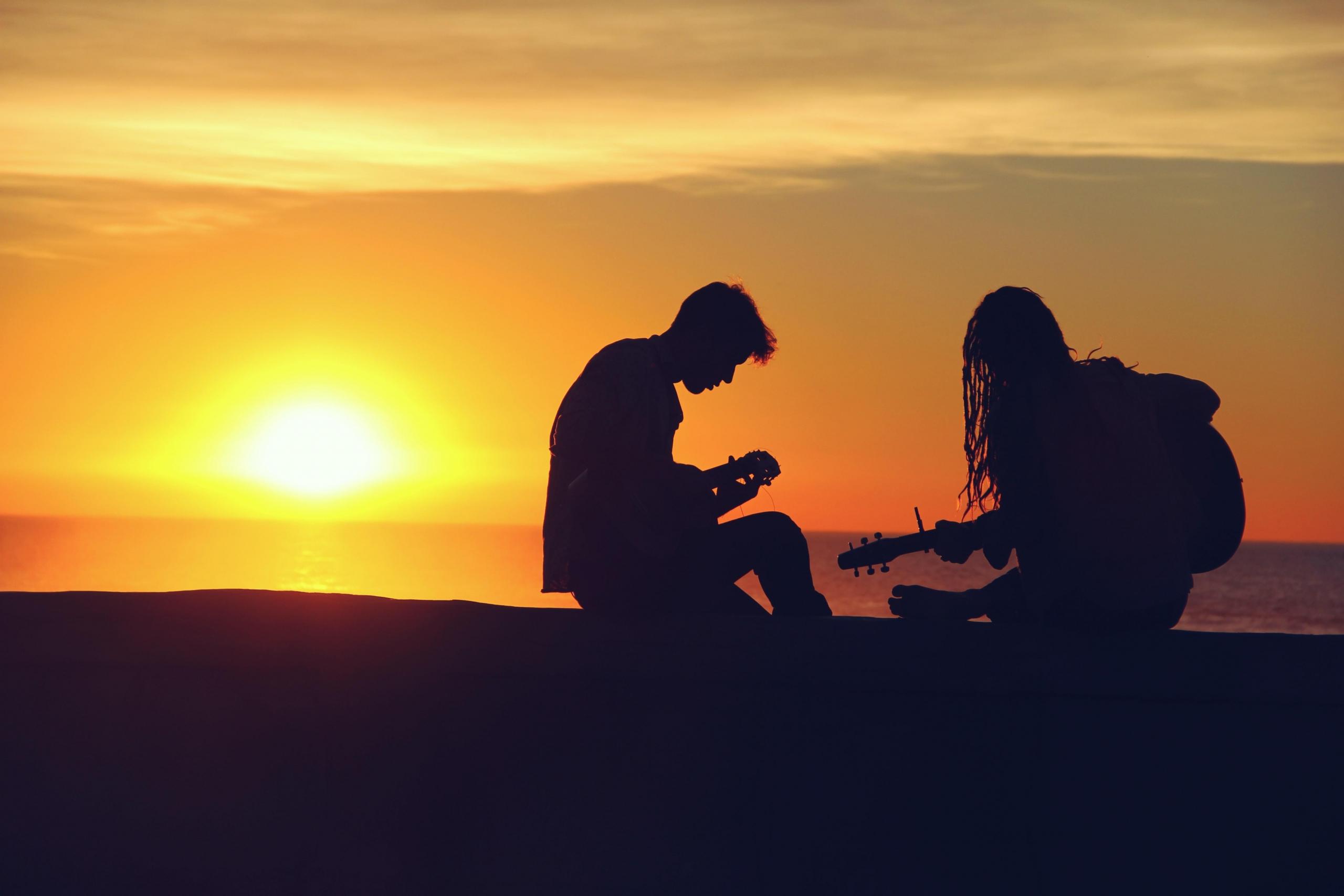 Ungdommer på strand i solnedgang spiller gitar.