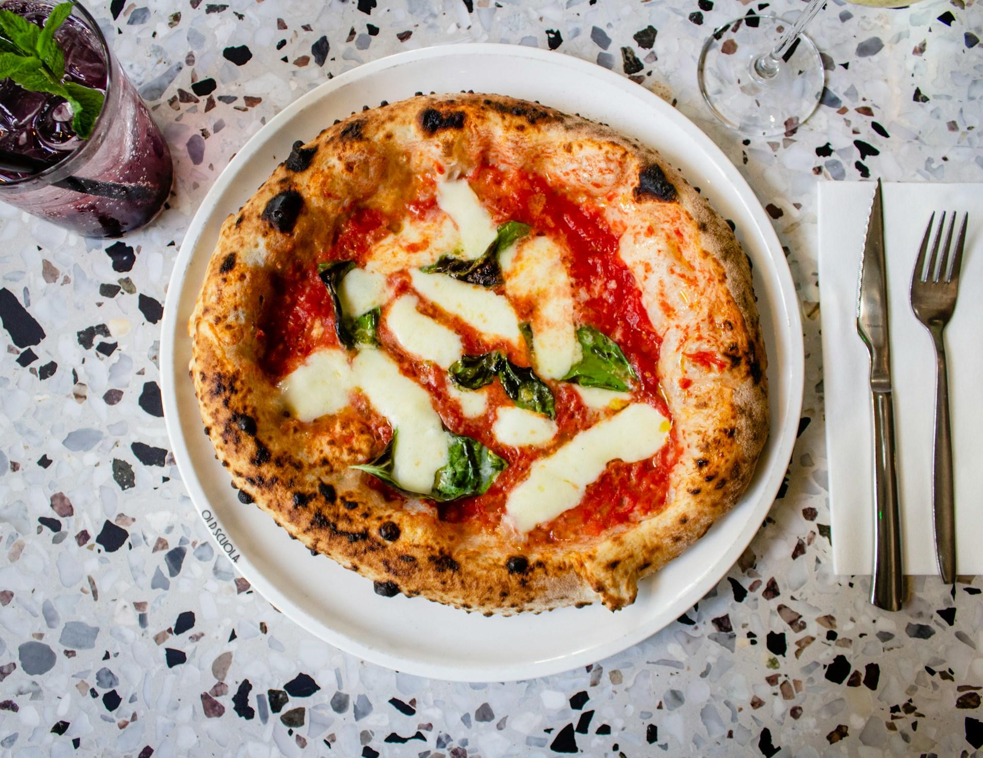 Italiensk pizza margherita på hvit tallerken med drikke og bestikk på hver side.