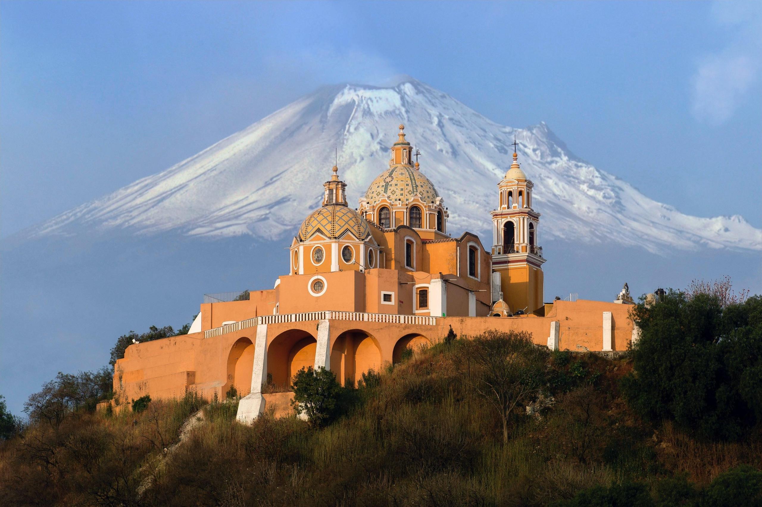 en oransje kirke ligger ved foten av noen fjell i mexico