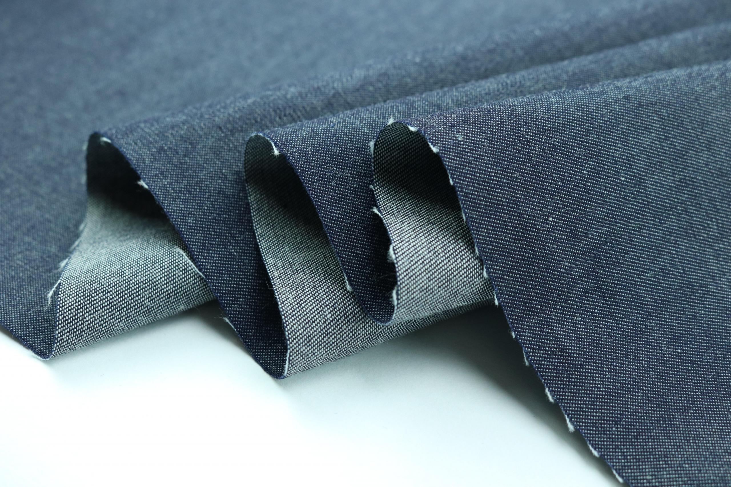 et mørkt, tynt jeansstoff ligger i folder på en hvit overflate, stoffet ser mykt ut