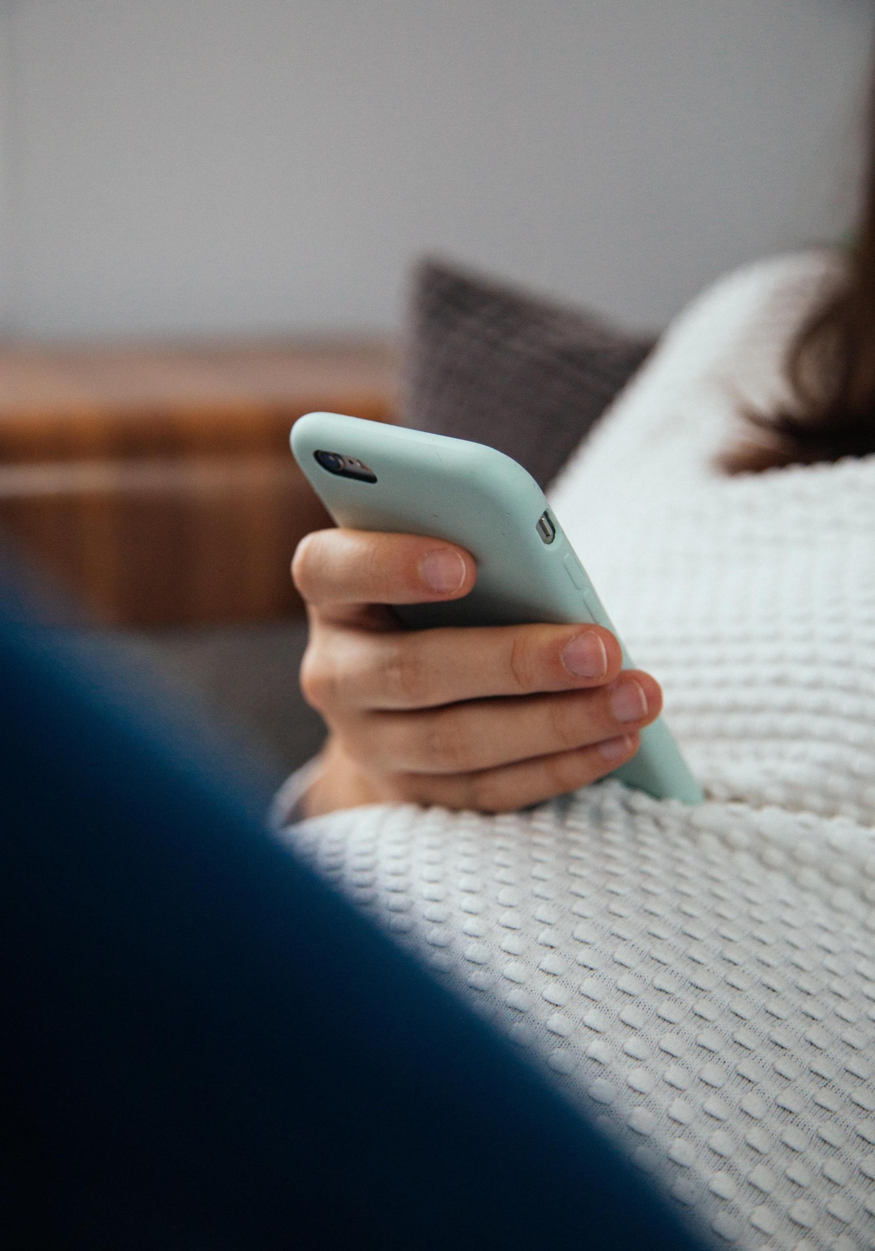 en person sitter lent tilbake og holder en mobil med grønt deksel