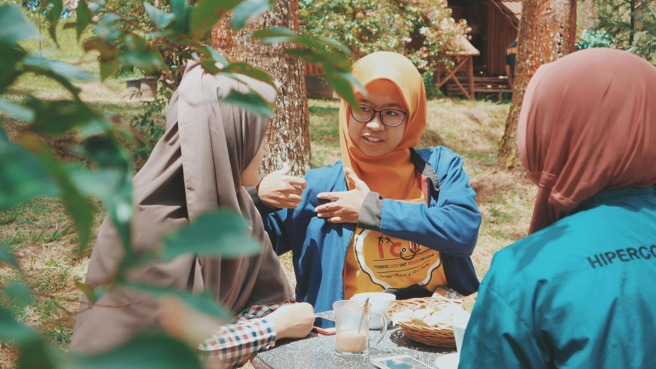 tre jenter sitter ved et bord ute i en hage, de snakker sammen, mat og drikke står på bordet