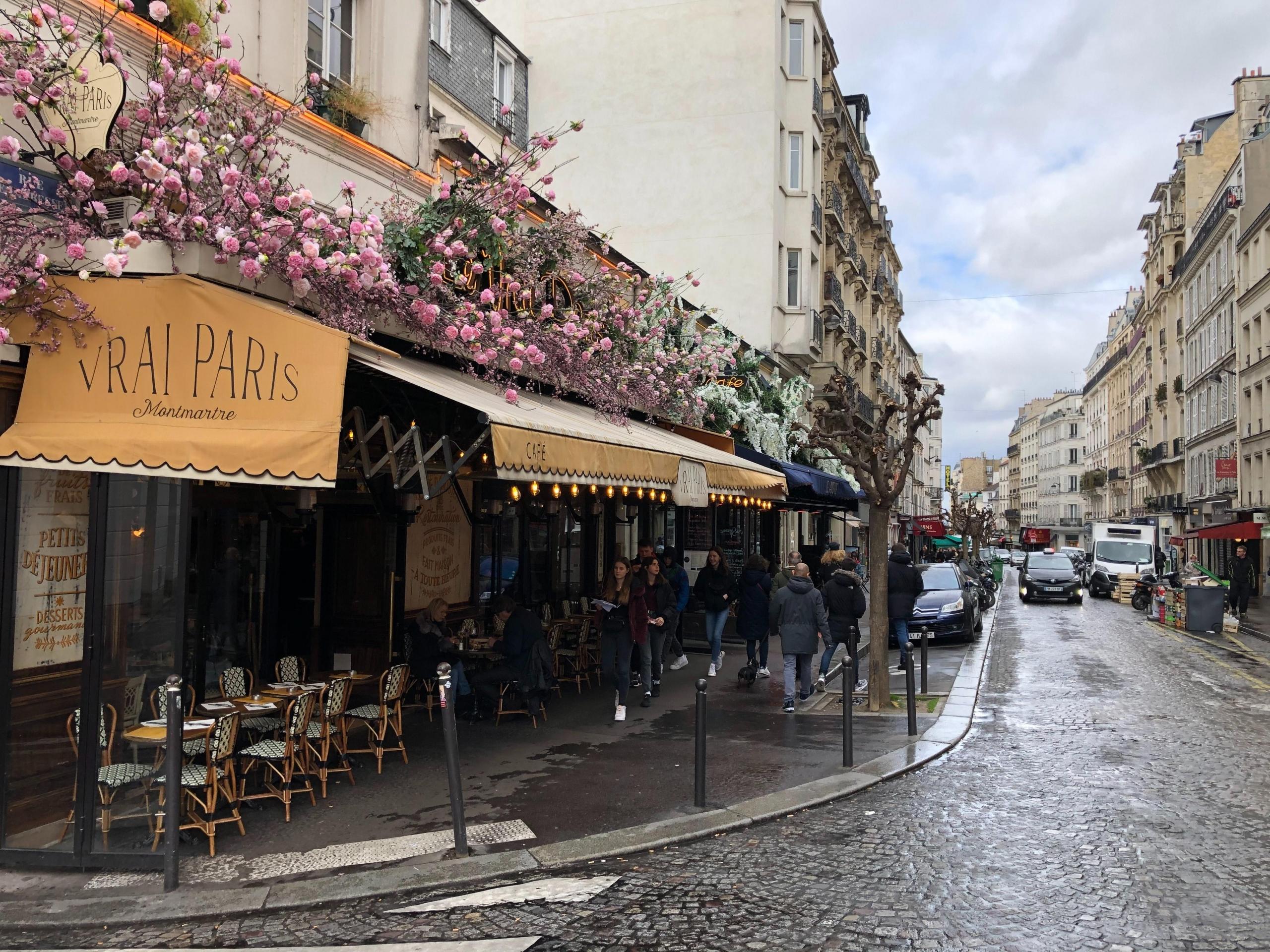 kafé i paris, det står stoler på fortauet, en gul persienne henger over dem, rosa blomster vokser over