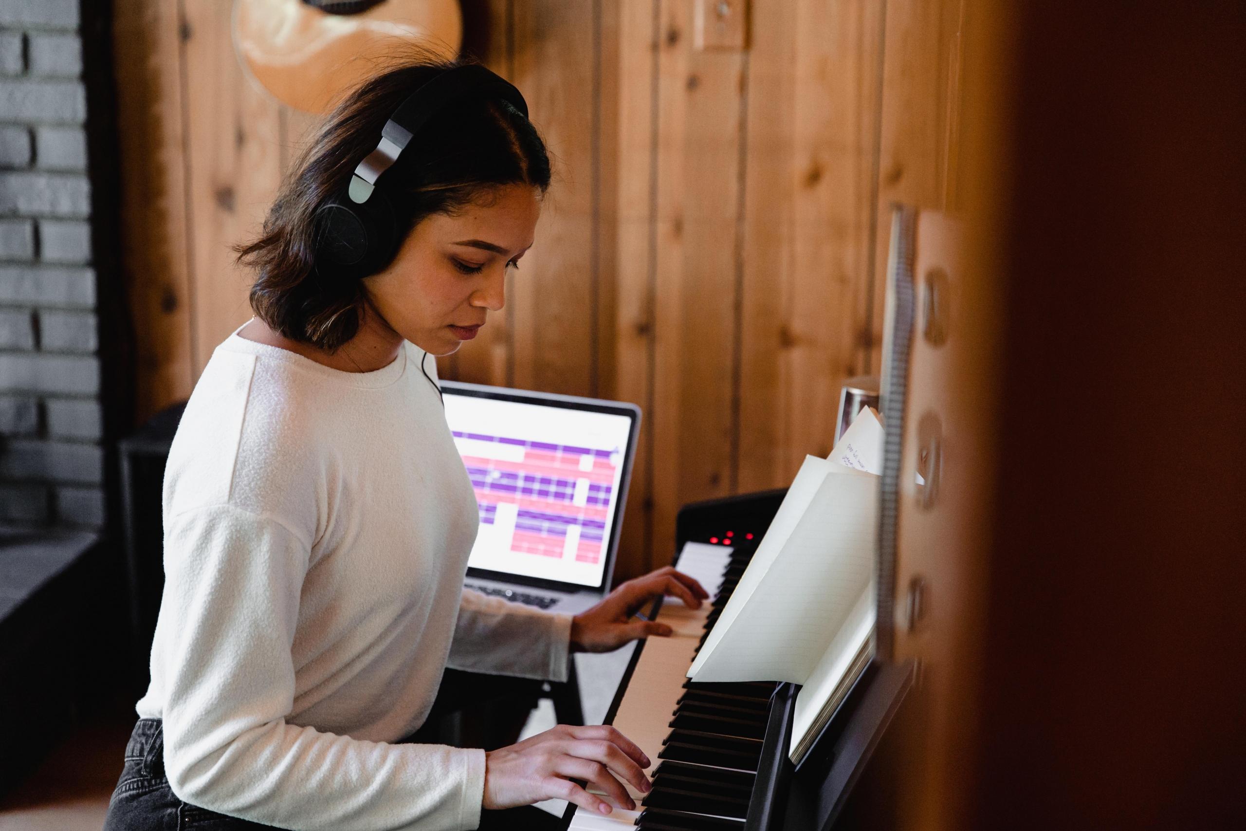 en kvinne med hodetekefoner spiller på et piano, i bakgrunnen står en laptop med et musikkmikseprogram