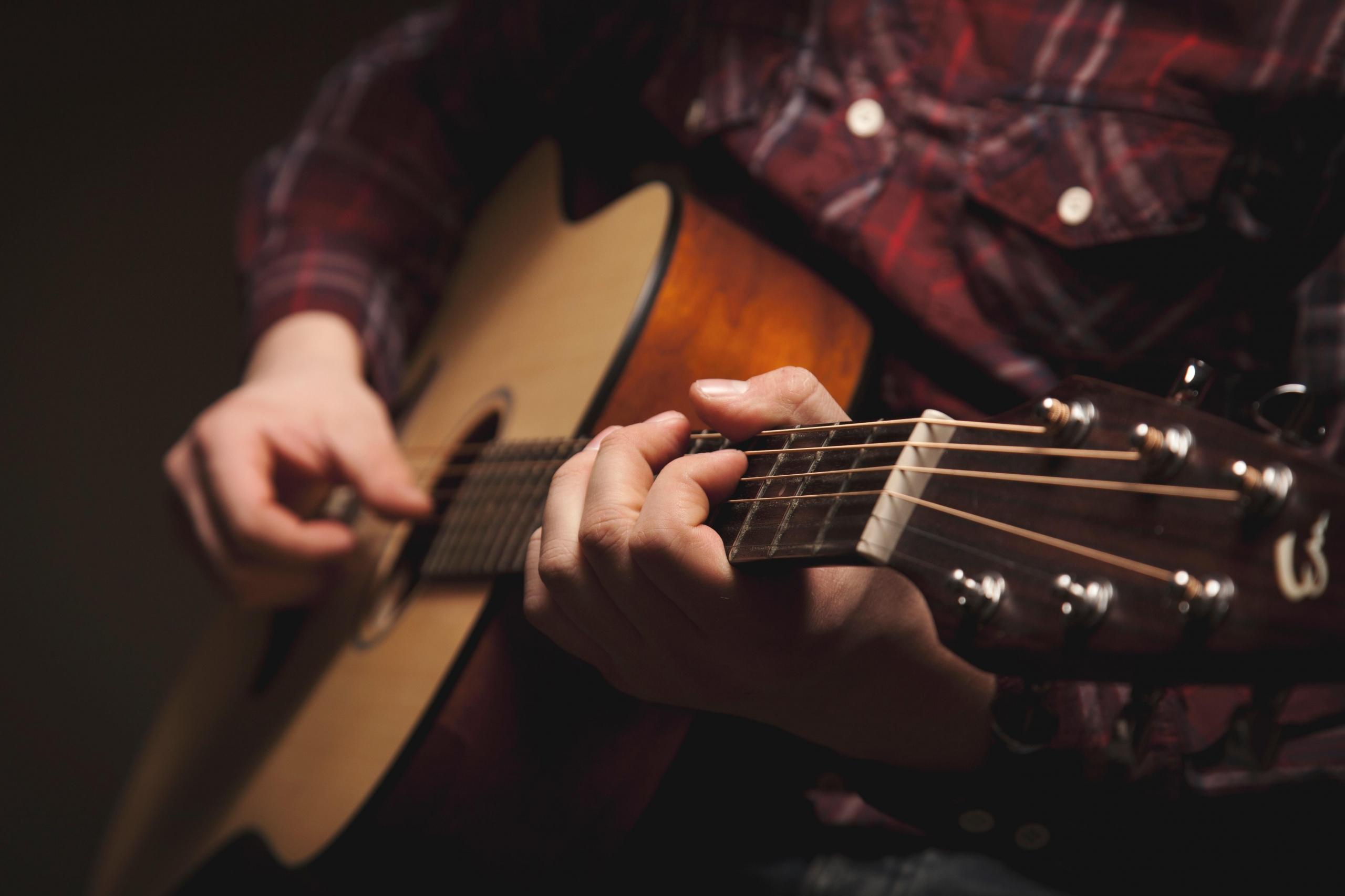 nærbilde av en gitar som spilles på av en mann i rød, rutete skorte i et dunkelt rom