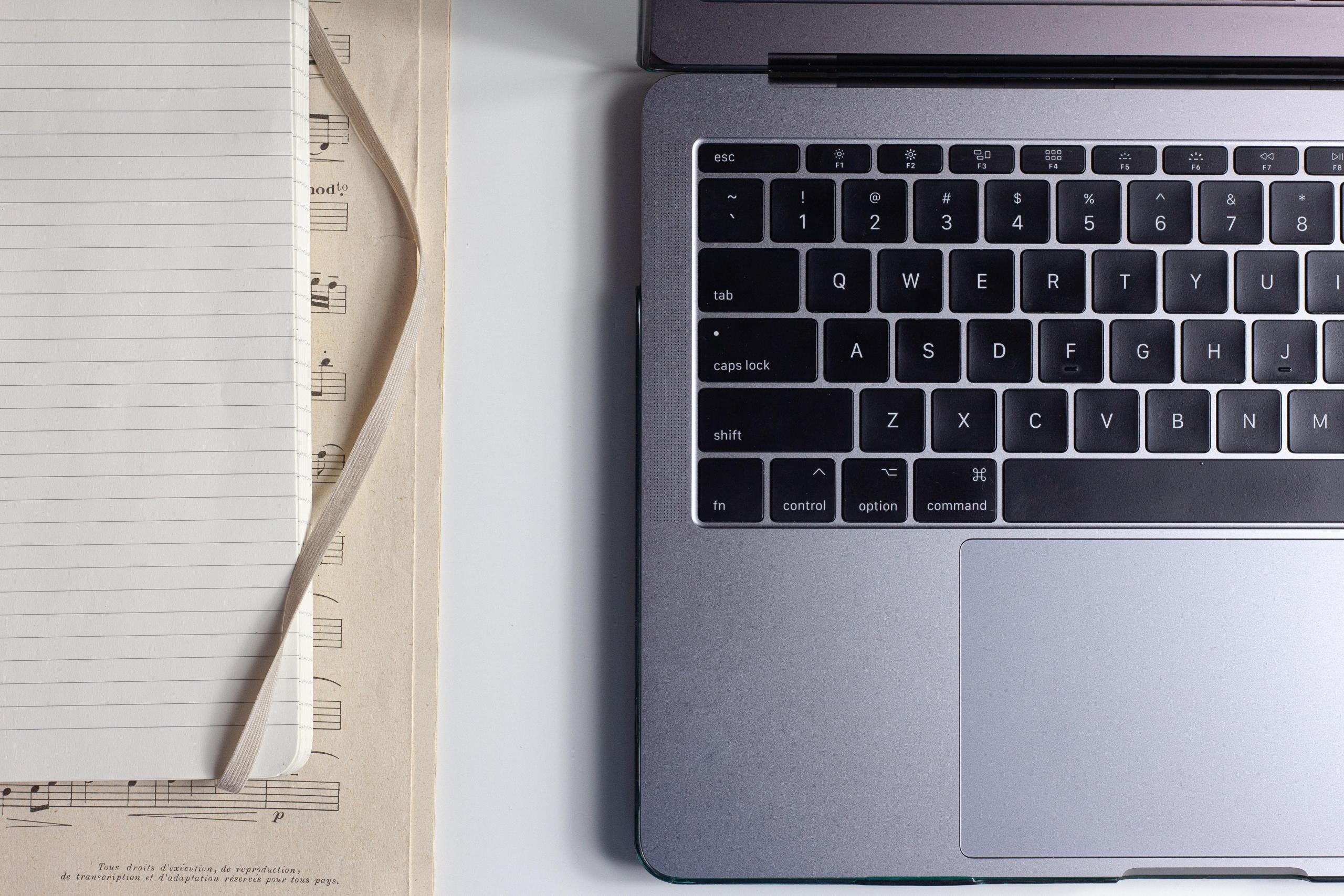 bilde ovenfra av tastaturet til en laptop, et noteark og en notatbok som ligger oppå notearket