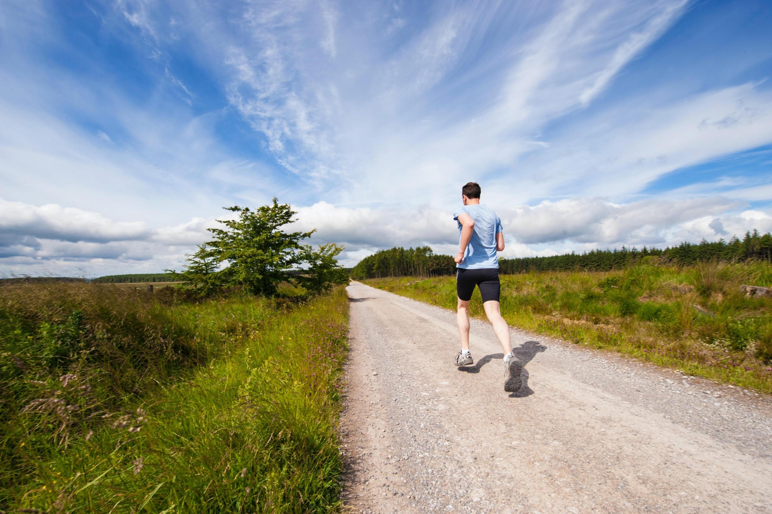 en mann jogger på en grusvei ved siden av en åker eller eng, i bakgrunnen er det trær