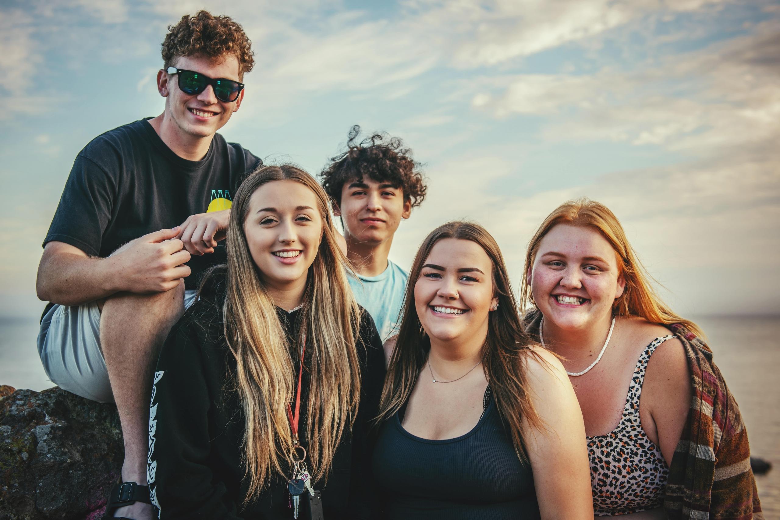 en gruppe venner smiler til kamera på en strand, de er unge