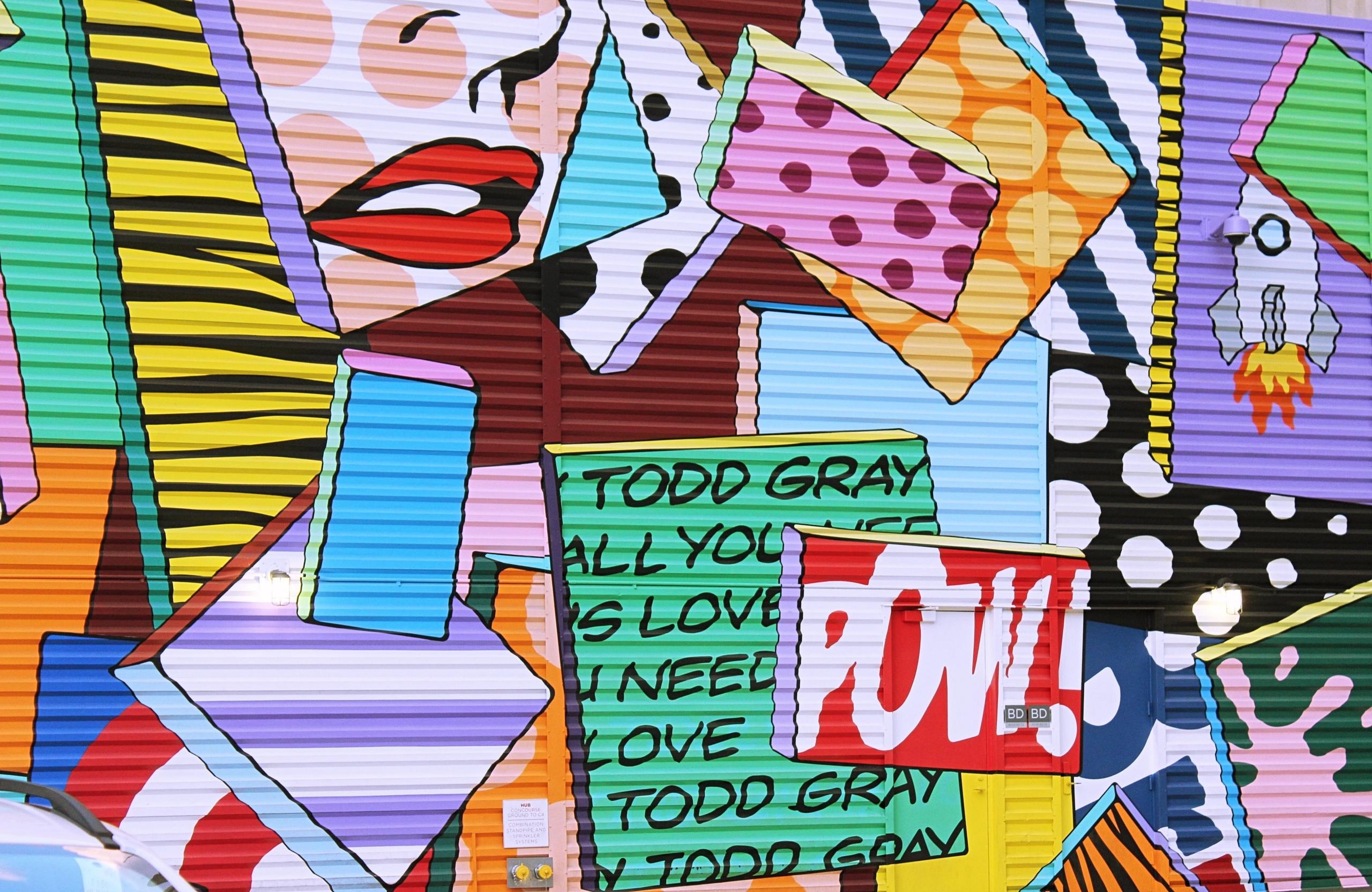 fargerik graffiti på en strukturvegg i New York, motivet er sterkt tegneserieinspirert, delt inn i overlappende ruter i sterke farger, blant annet av en kvinnes nese og munn og lydhermende ord