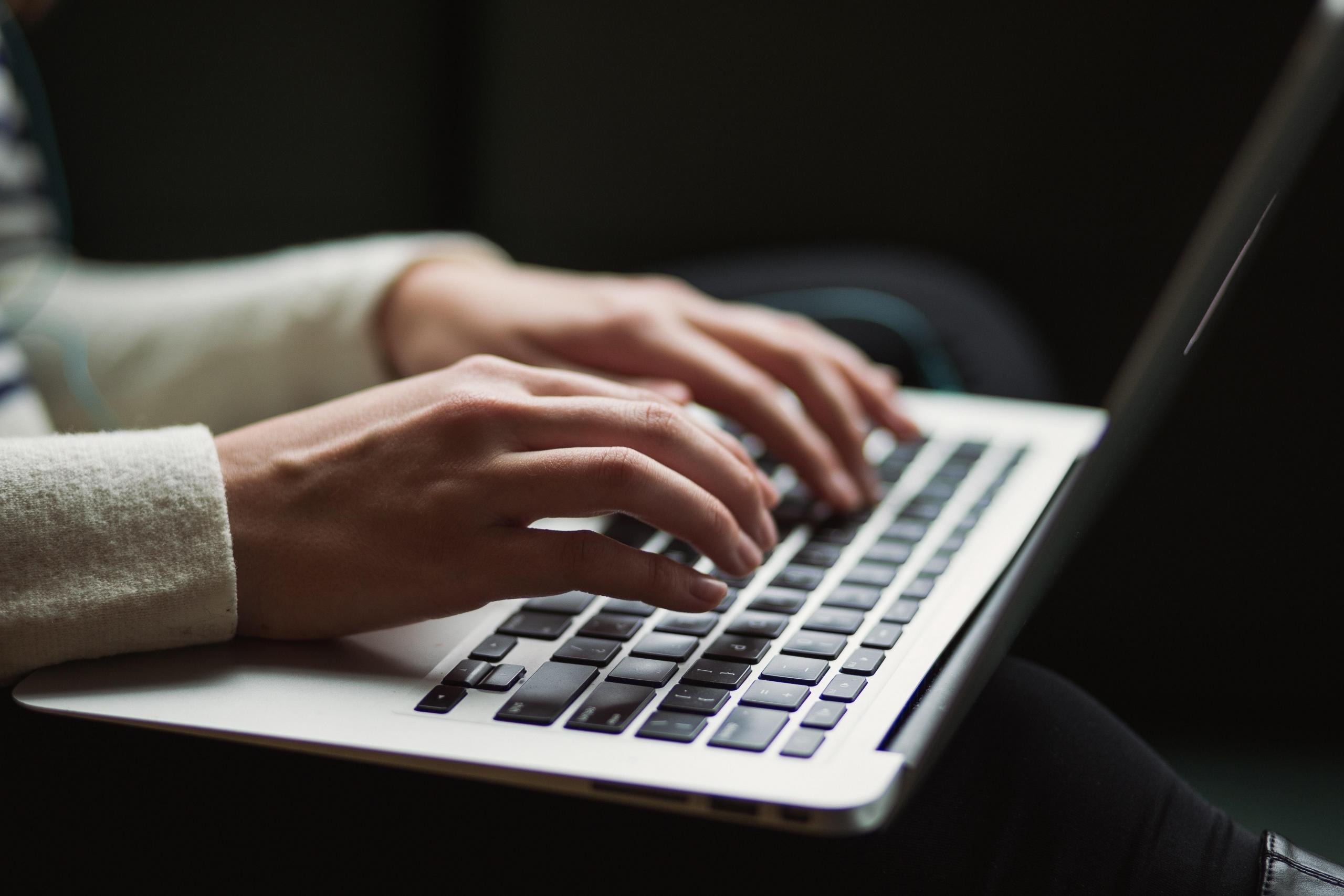 nærbilde av hender som skriver på tastaturet på en laptop, personen har på seg en pusete hvit genser