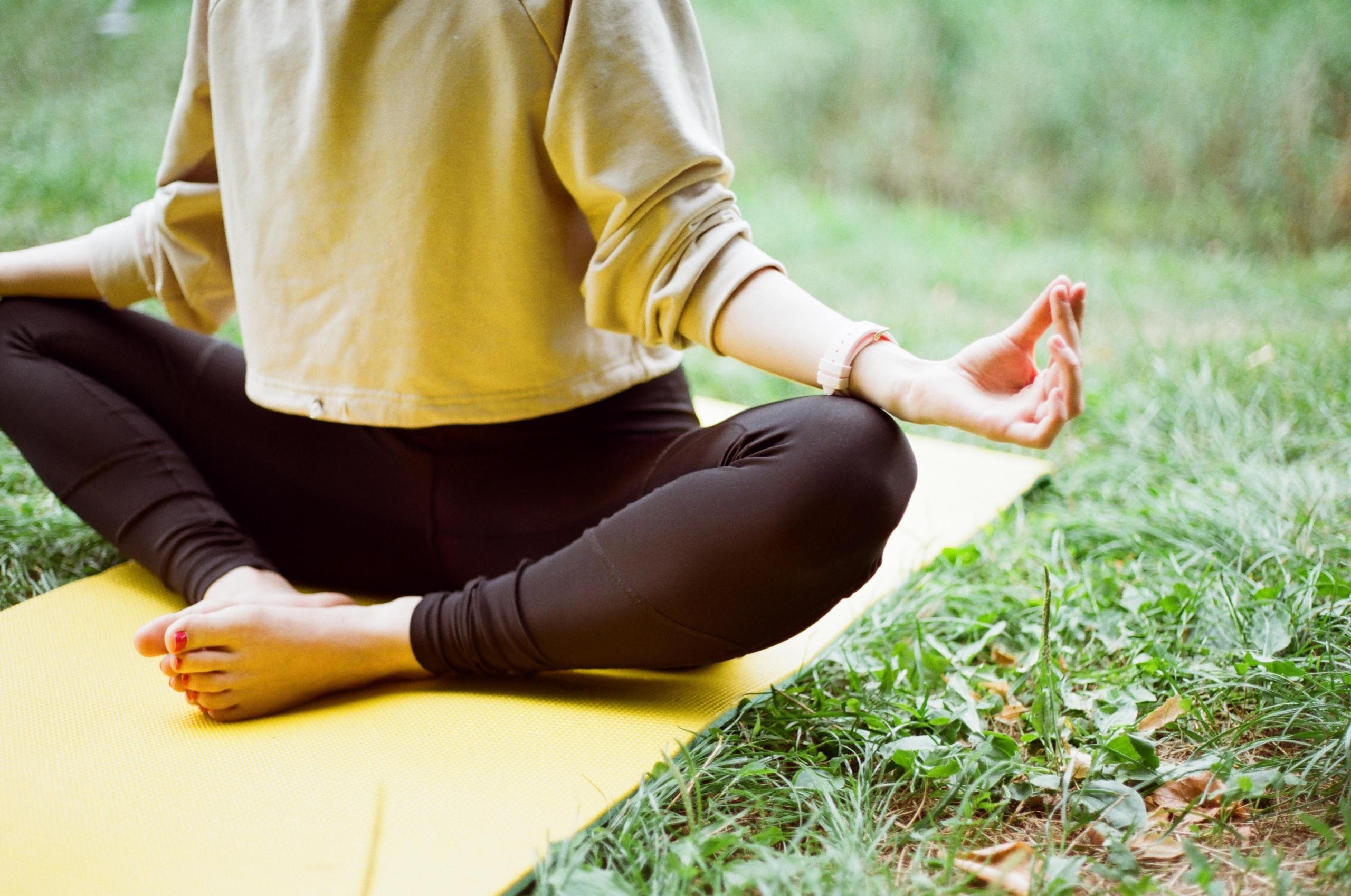 person sitter i mediterende stilling på en yogamatte på gress, hun har på en vid genser