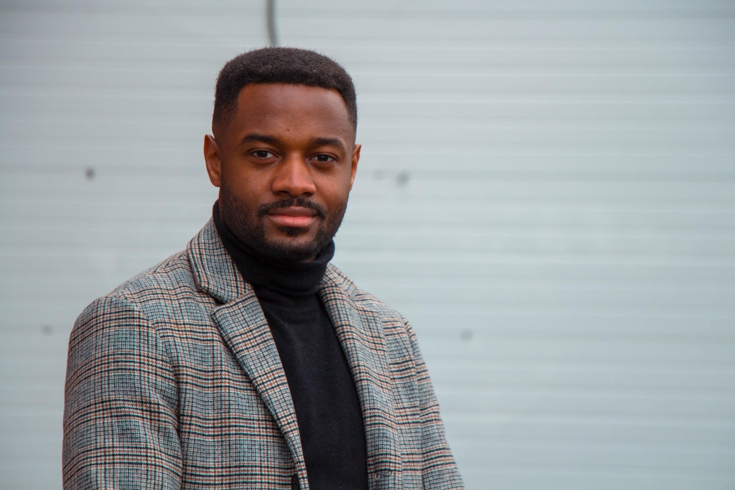 en mann i svart turtleneck og rutete grå dressjakke ser i kamera
