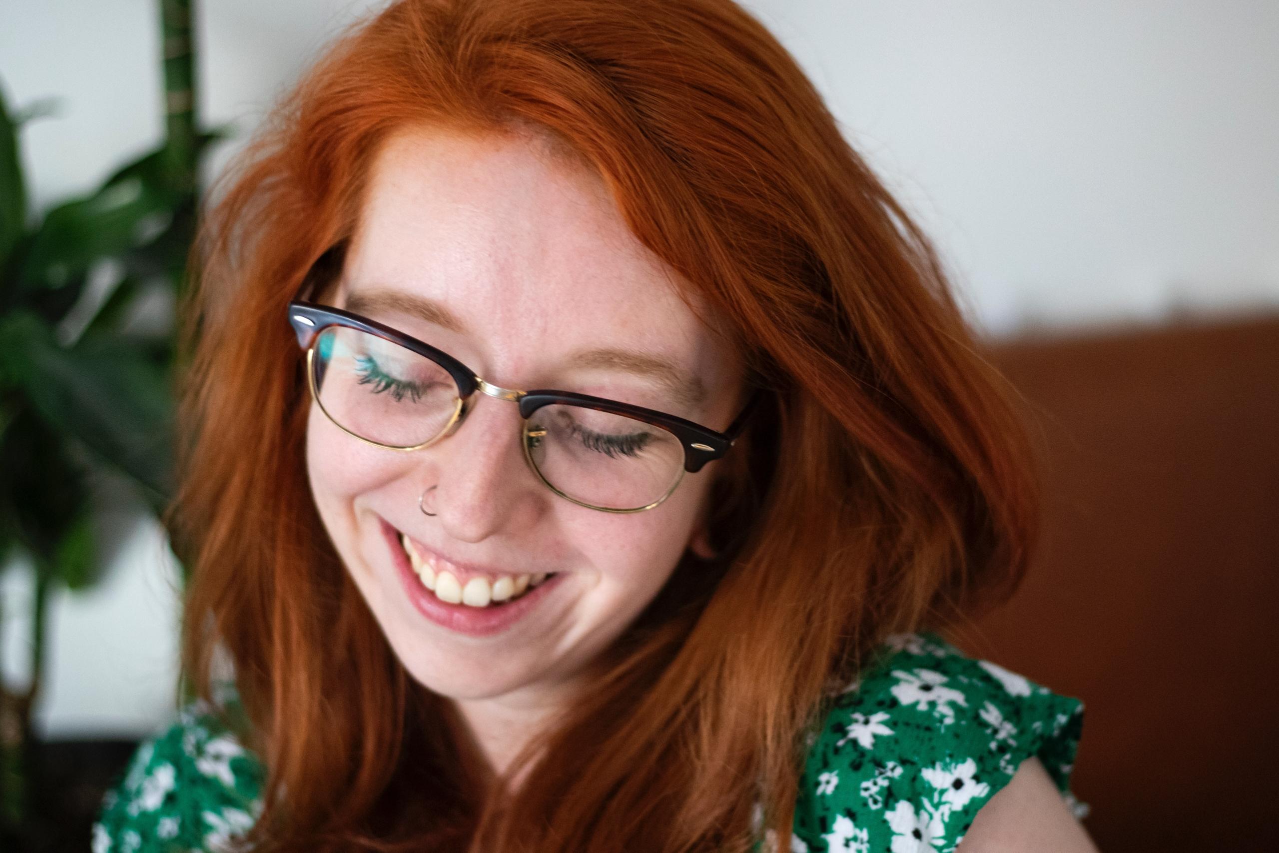 en rødhåret jente med briller ler og ser ned