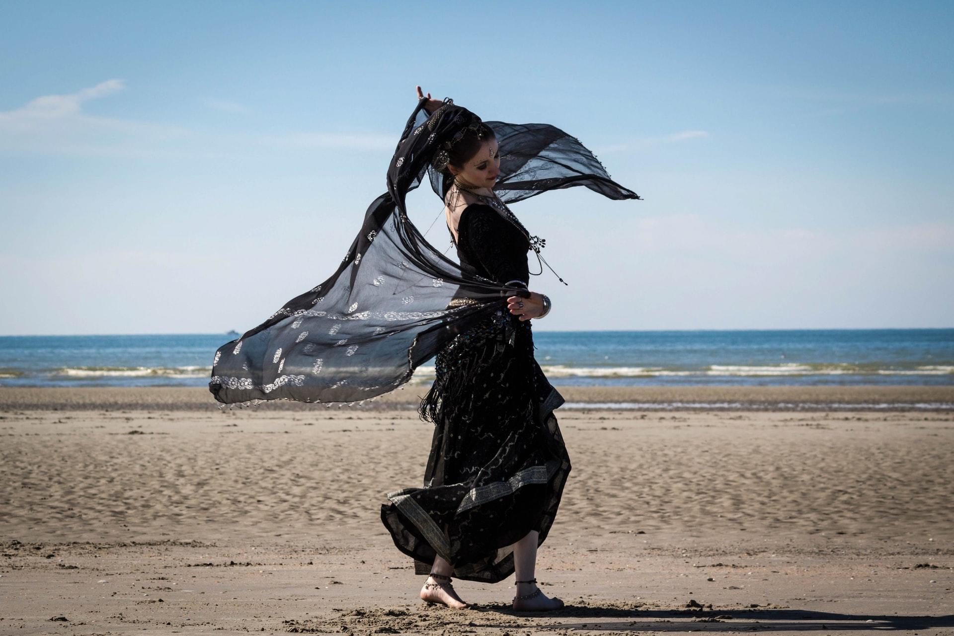 Magedanser med svart kjole og slør, på en strand