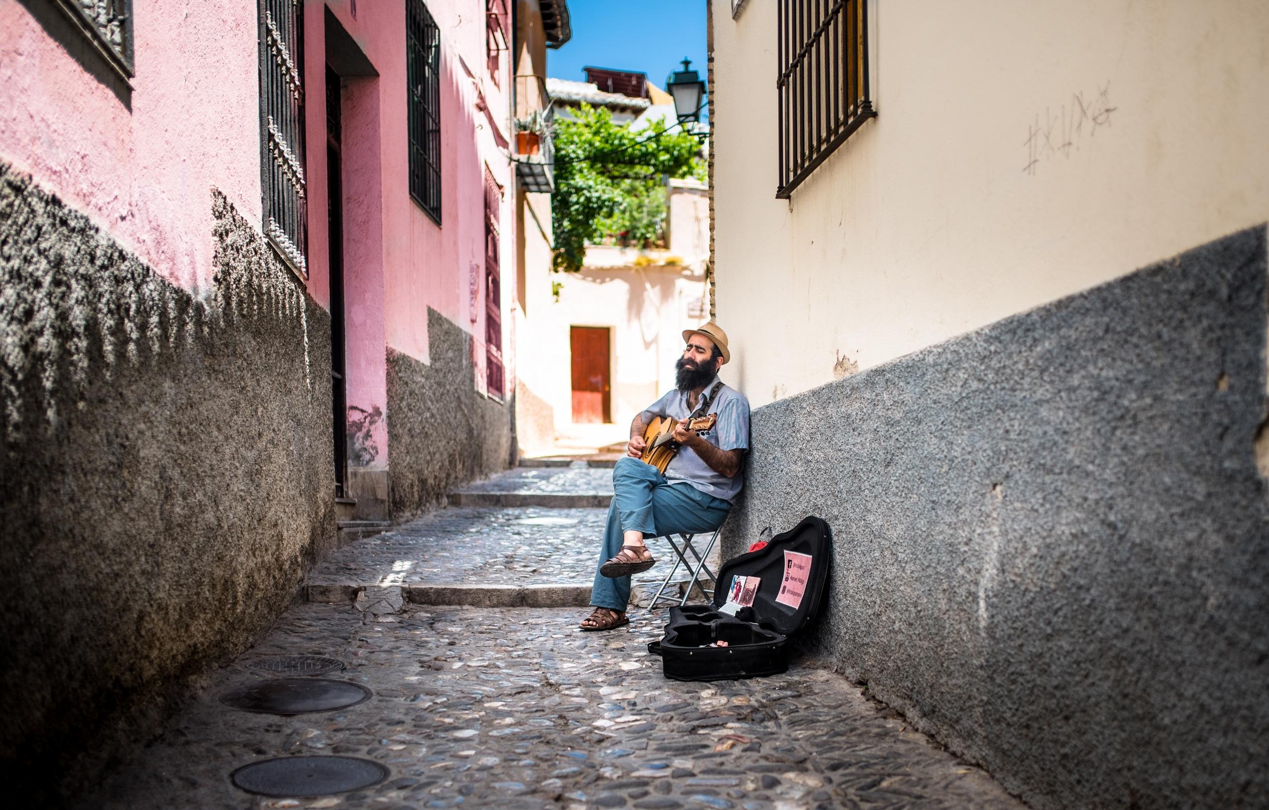 en gatemusikant sitter på en stol i en smal gate og spiller gitar