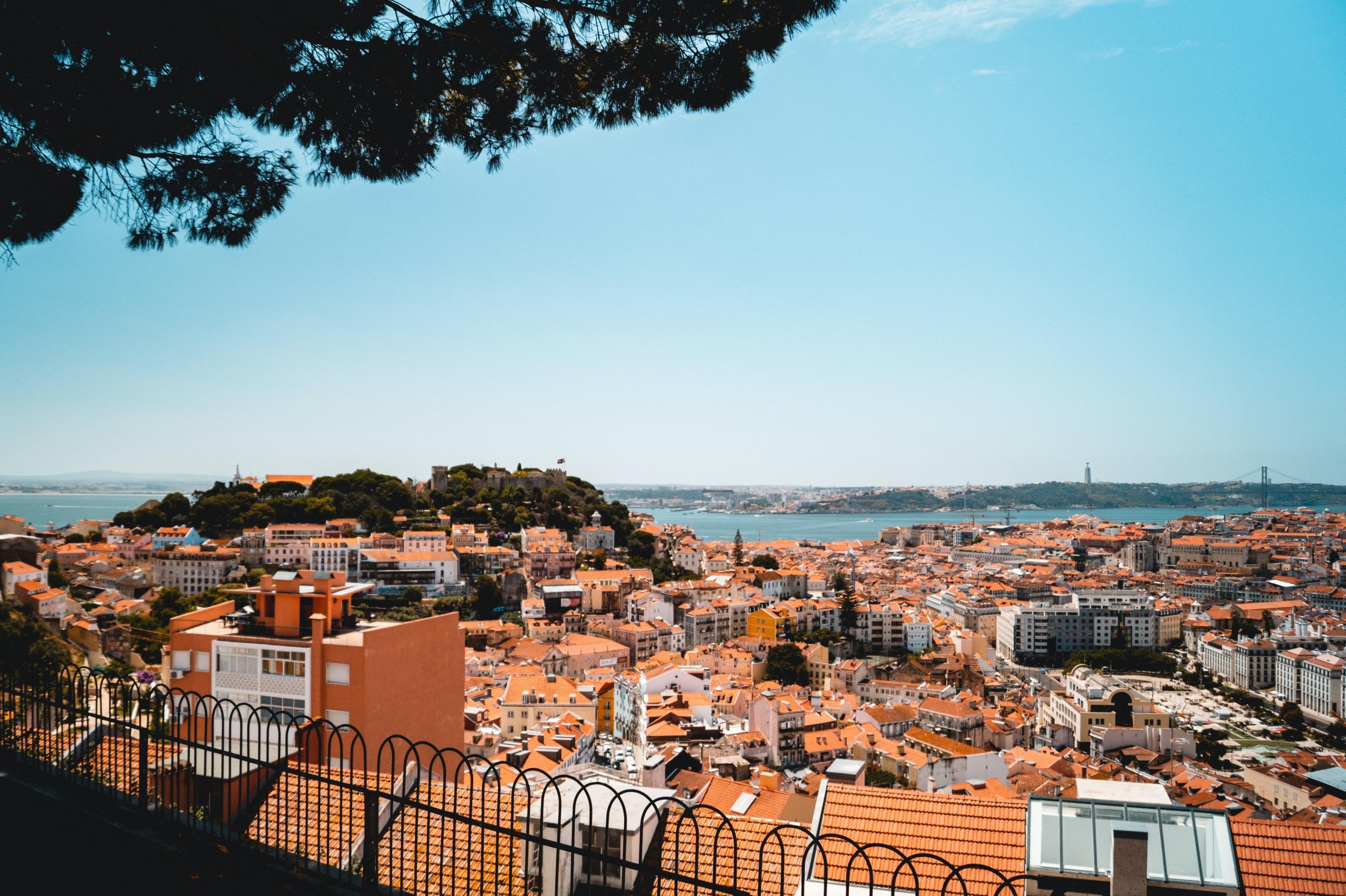 bilde av lisboa fra en høyde, rødbrune hustak og kyst i bakgrunnen