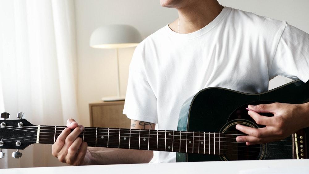 Person i hvit t-skjorte som spiller gitar