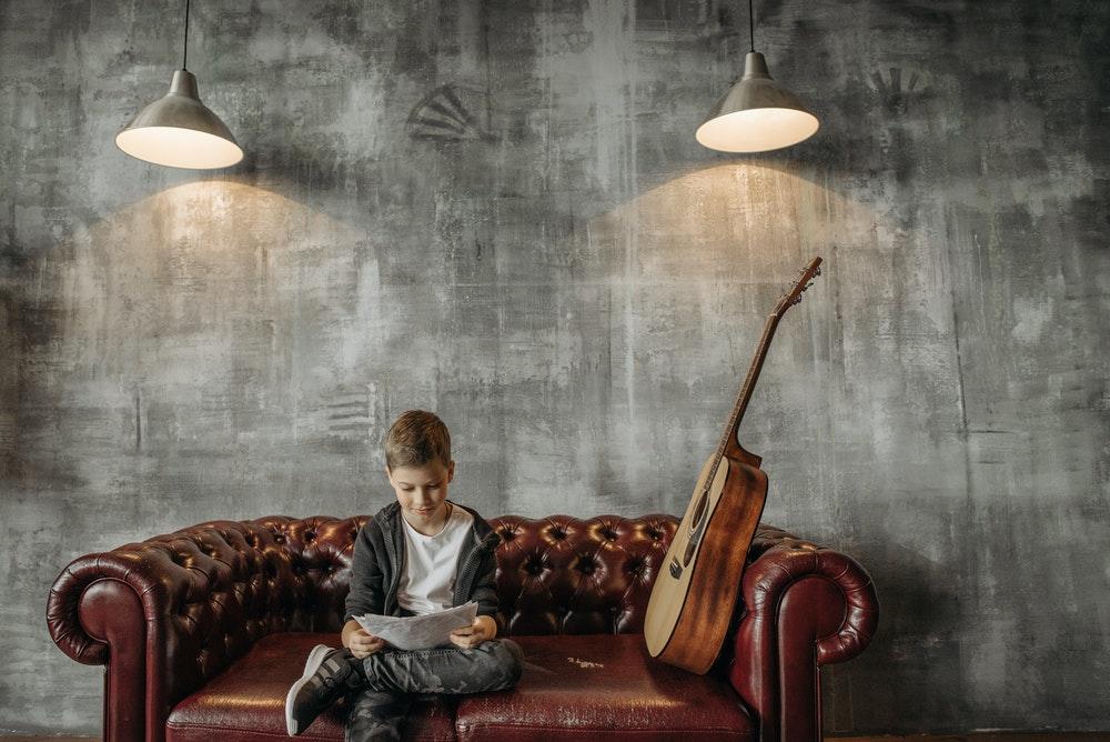 Gutt som sitter i en sofa med en gitar