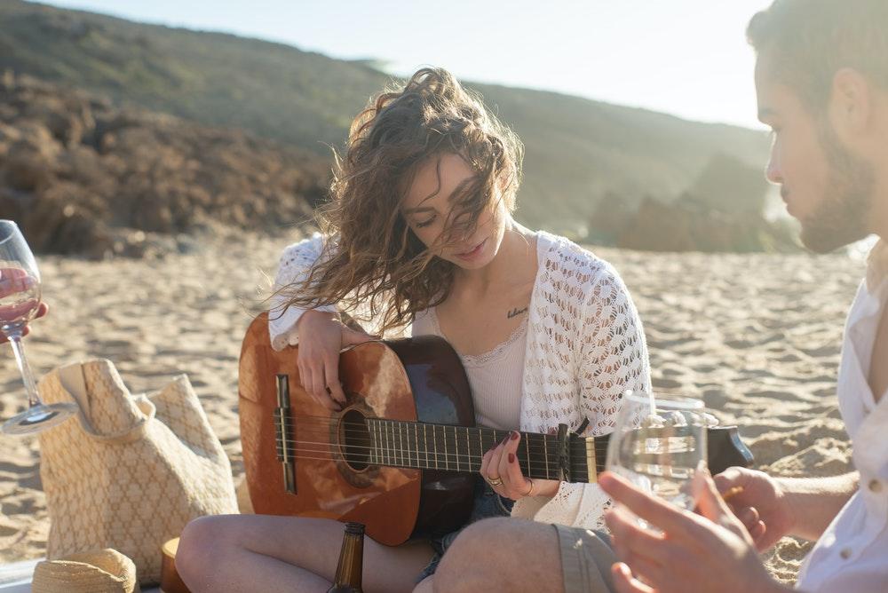 Kvinne som spiller gitar ute på en strand