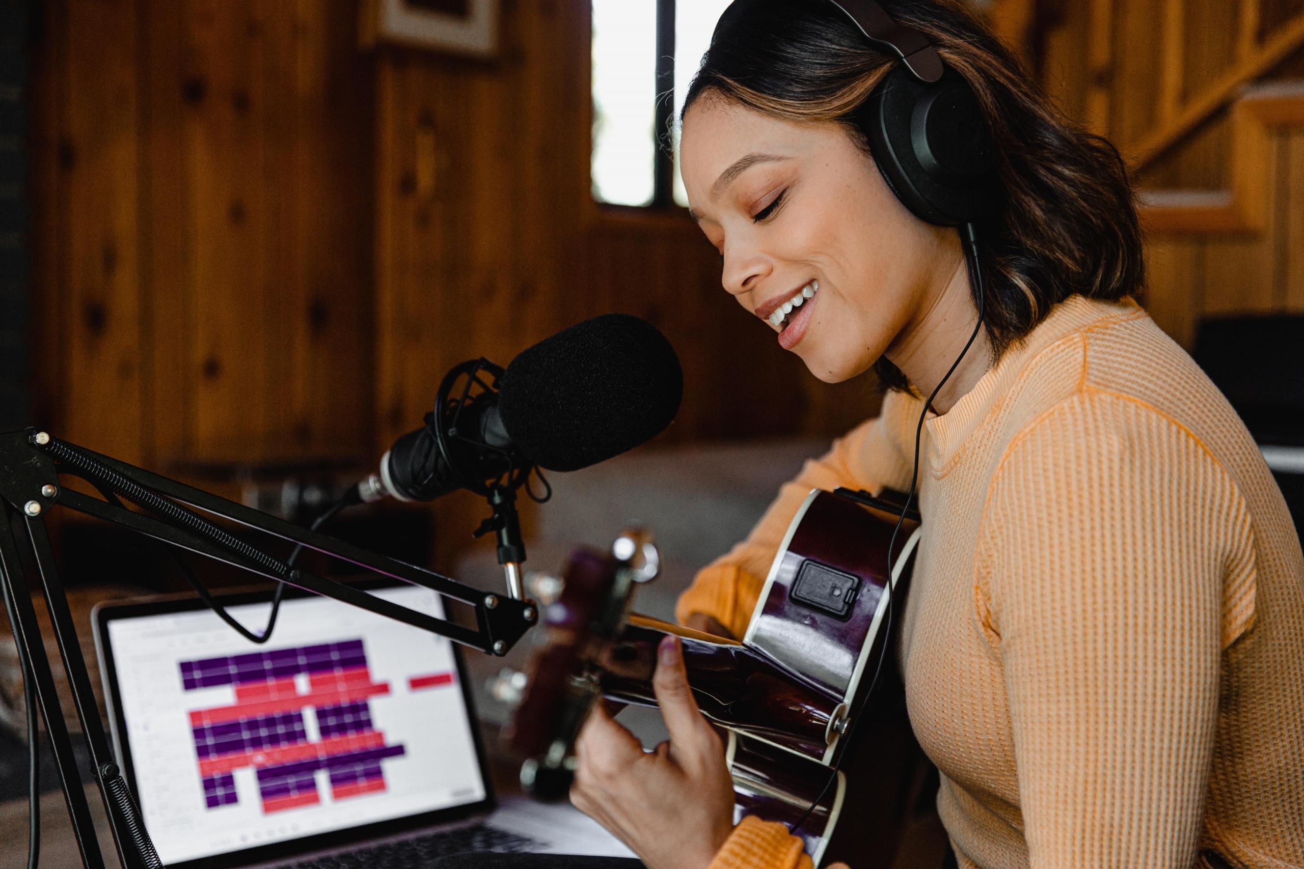 en kvinne synger og spiller gitar ved en pc med et musikkprogram