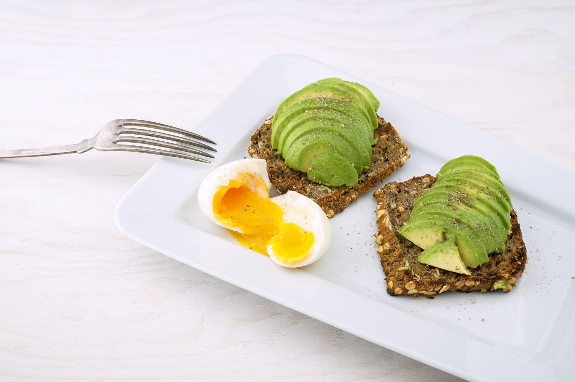 En gaffel og hvit tallerken med brød med avokado og egg på