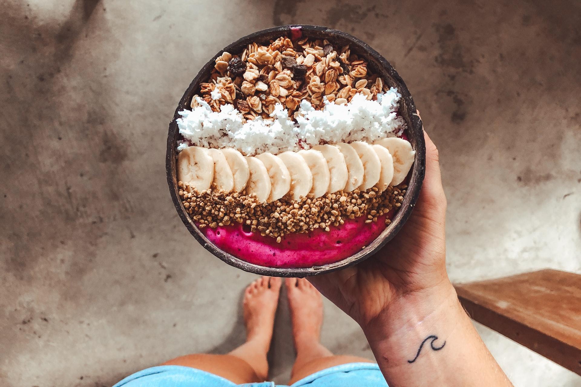 En person som holder en smoothiebowl med banan og nøtter