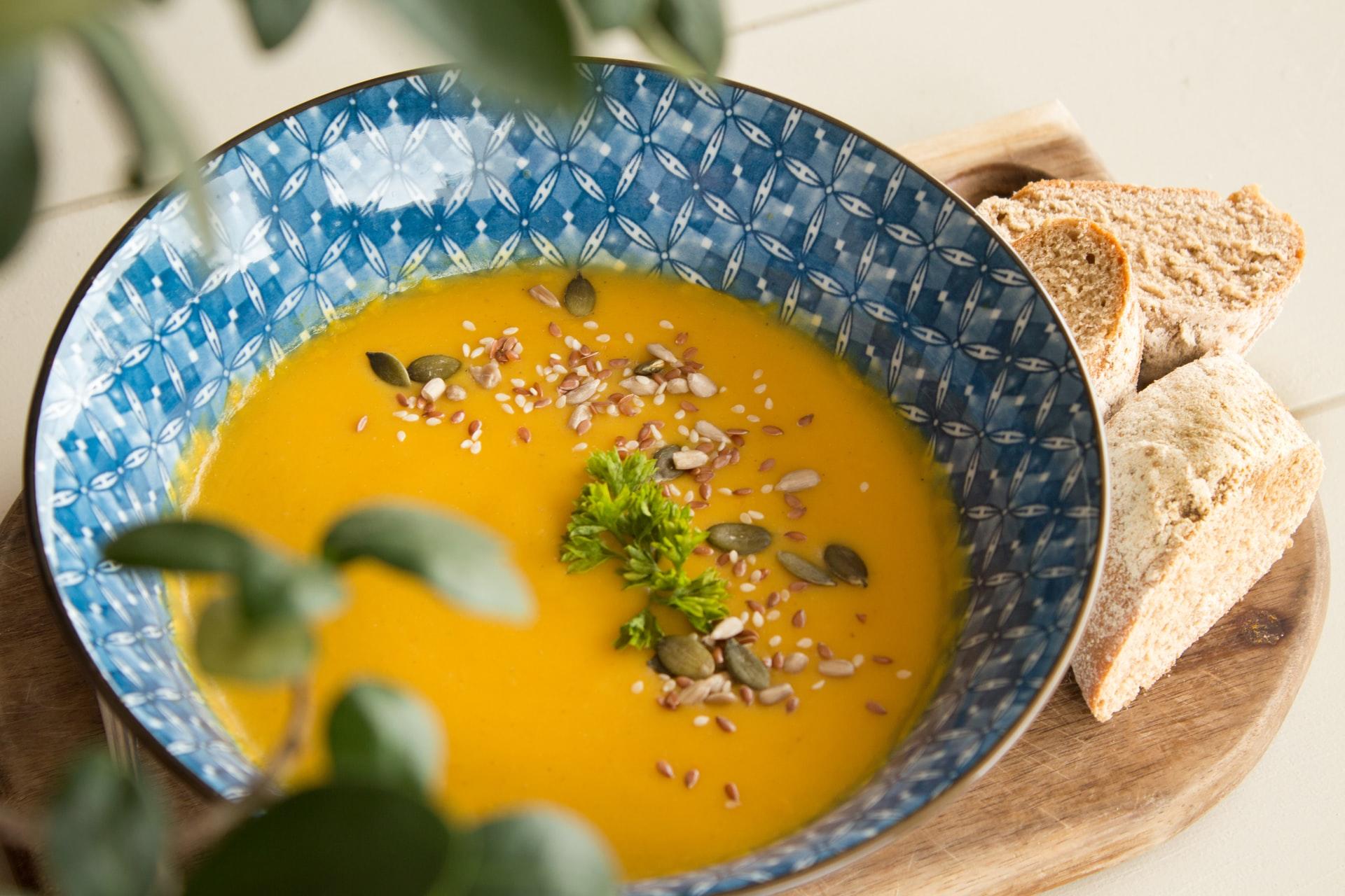 Gul suppe i en blå skål med brød på siden
