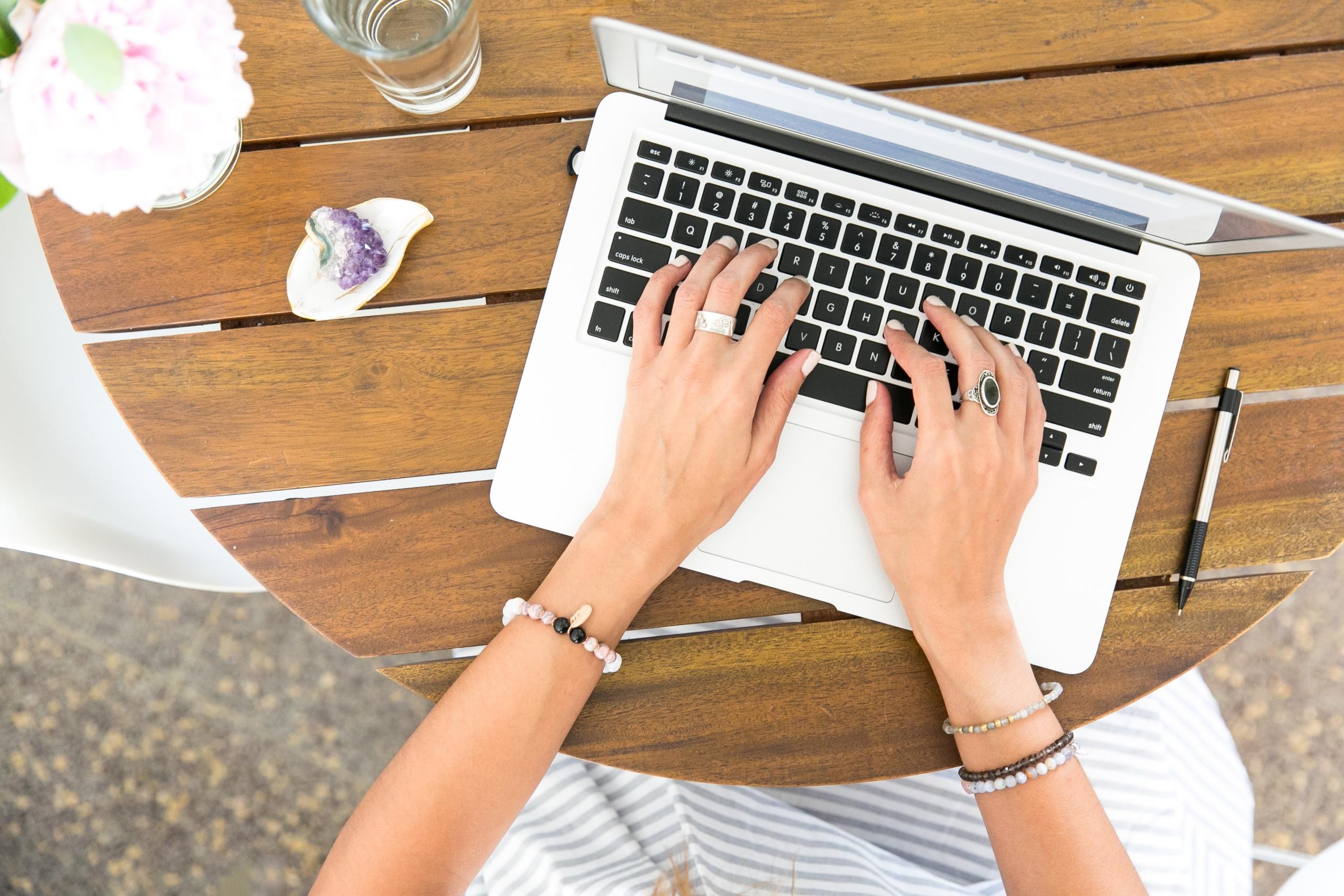 en person med mange ringer og armbånd skriver på en laptop