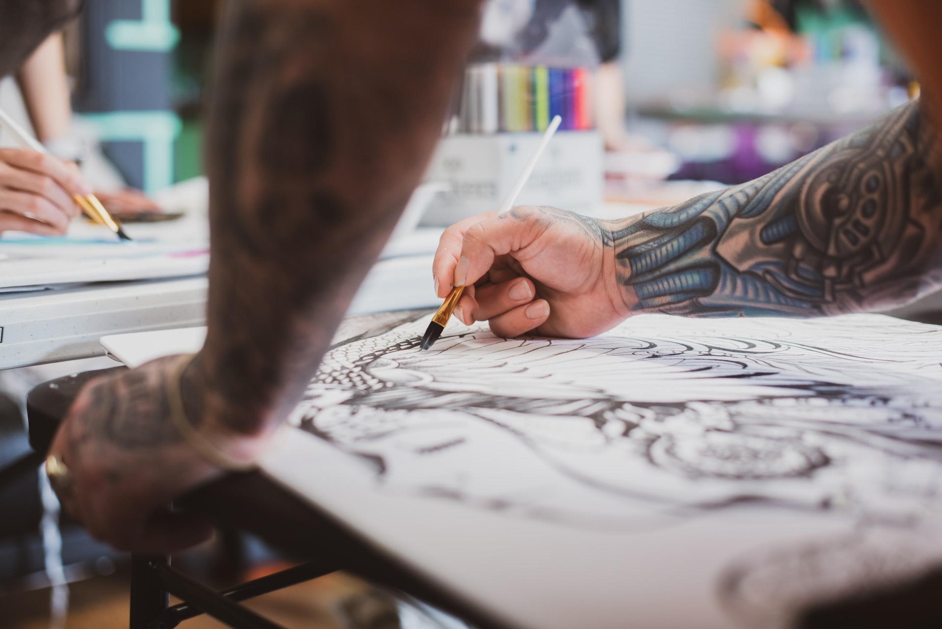 Person med tatoveringer som tegner et design