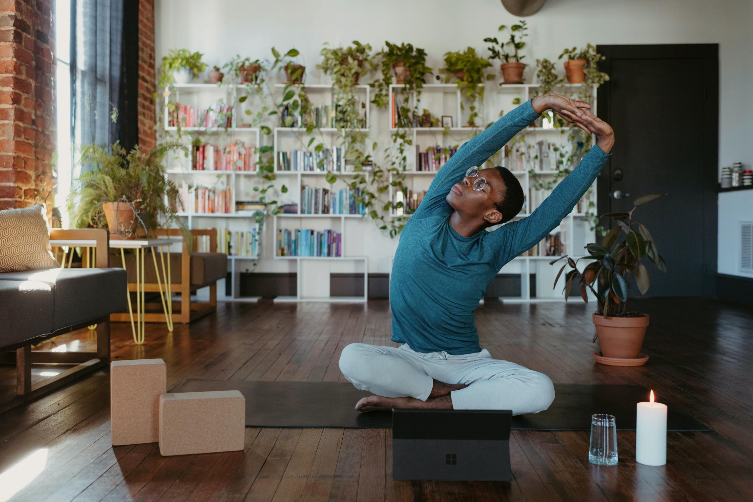 en mann sitter på en yogamatte med beina i kors og strekker seg, et nettbrett er stilt opp foran ham