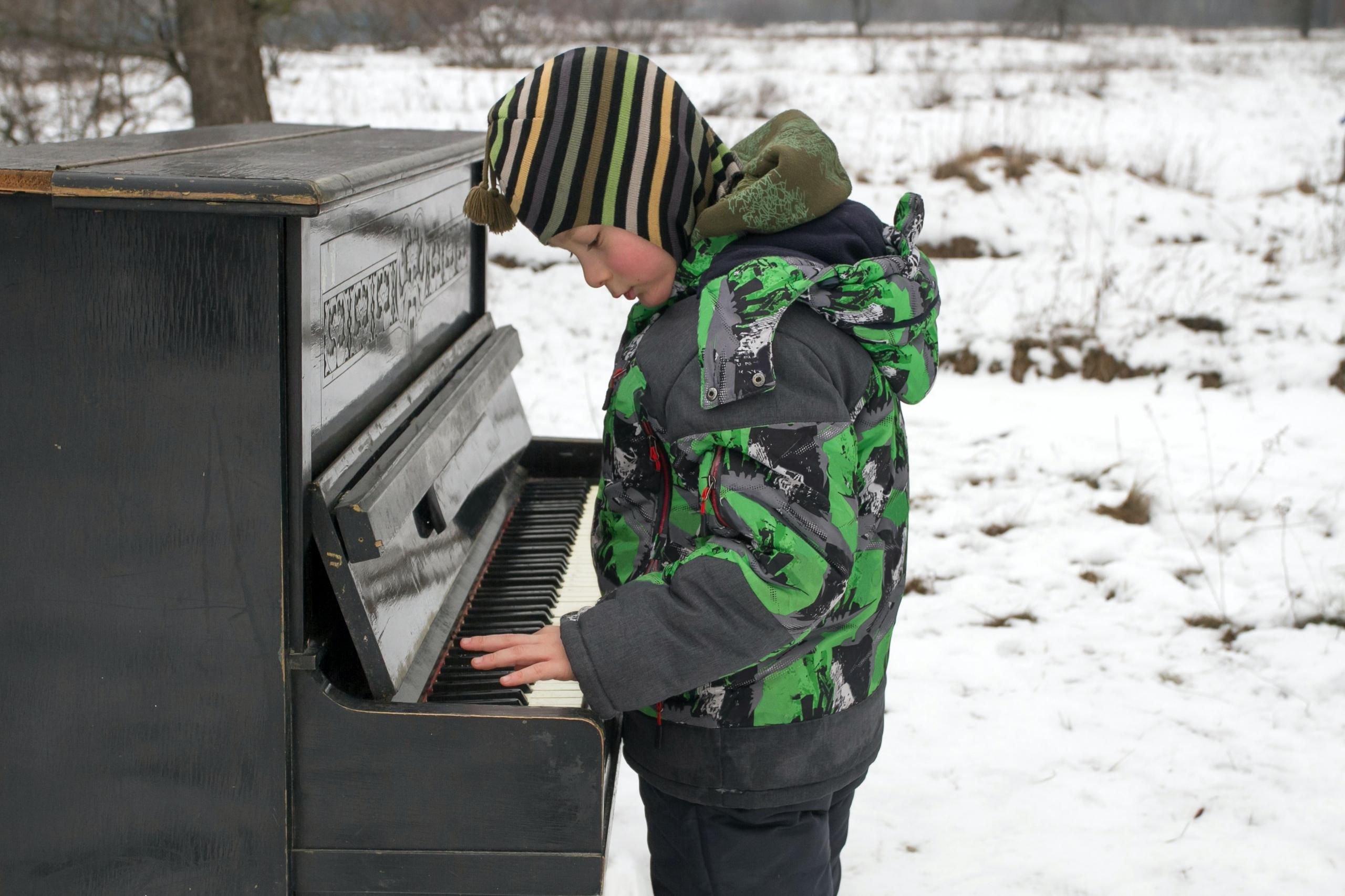 en ung gutt spiller på et piano ute, han ser konsentrert ut