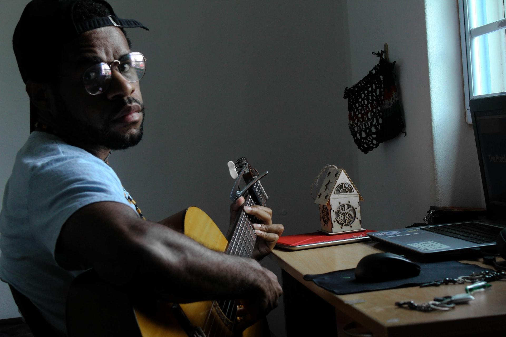 En mann som spiller gitar og har en pc foran seg
