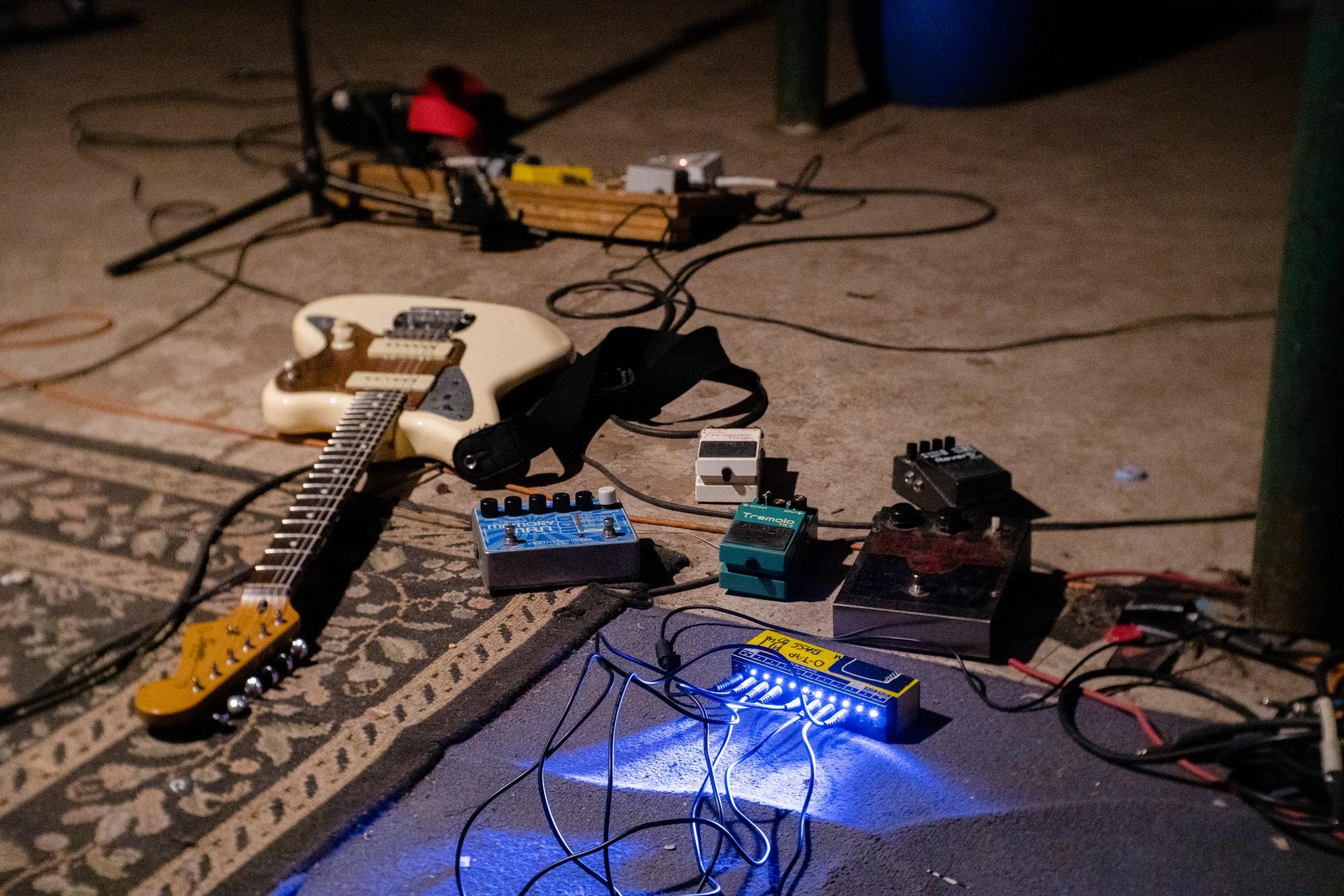 Et gulv med en hvit elektrisk gitar og ulikt gitarutstyr