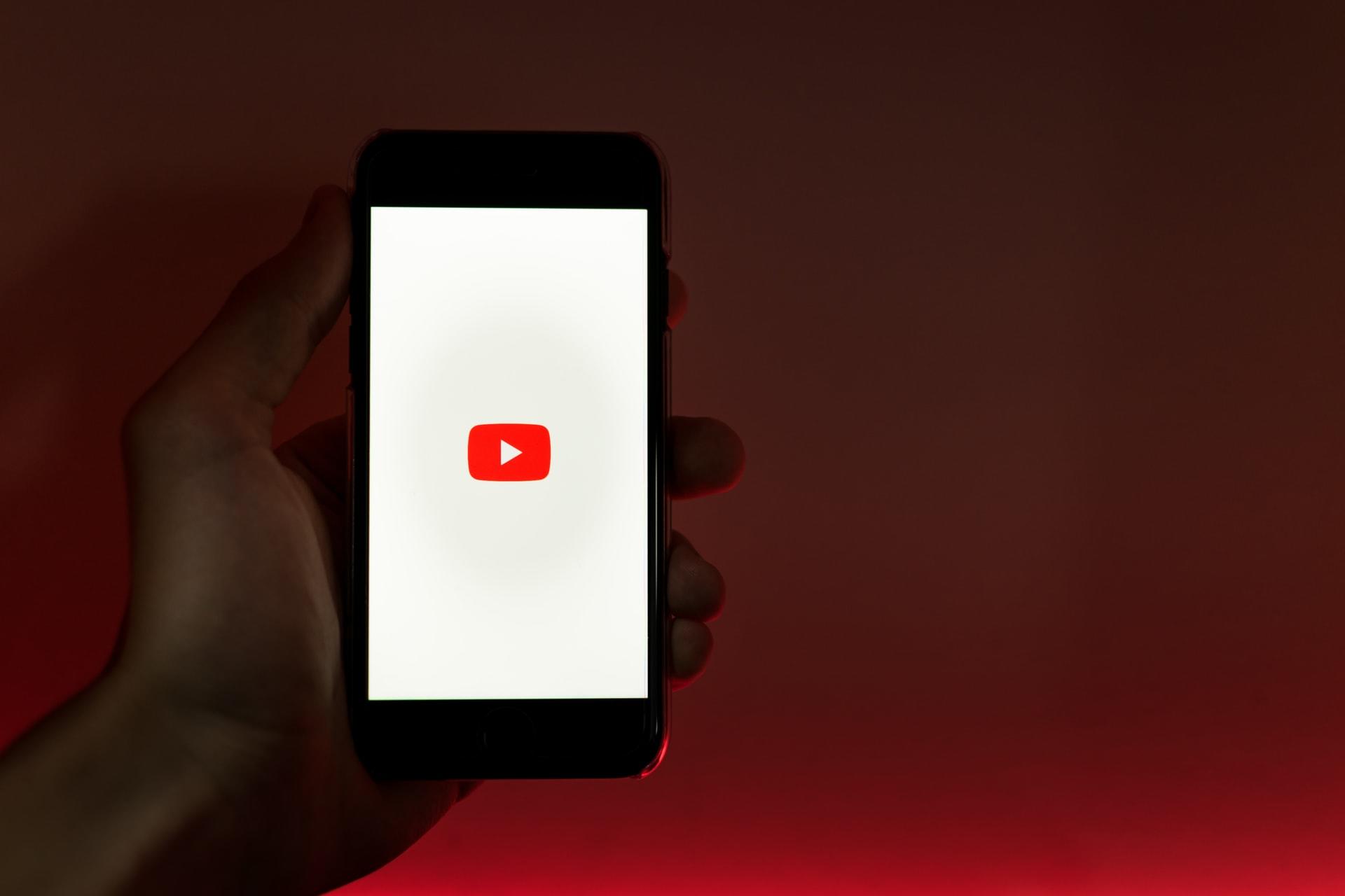En hånd som holder en mobil med Youtube-logoen og hvit bakgrunn