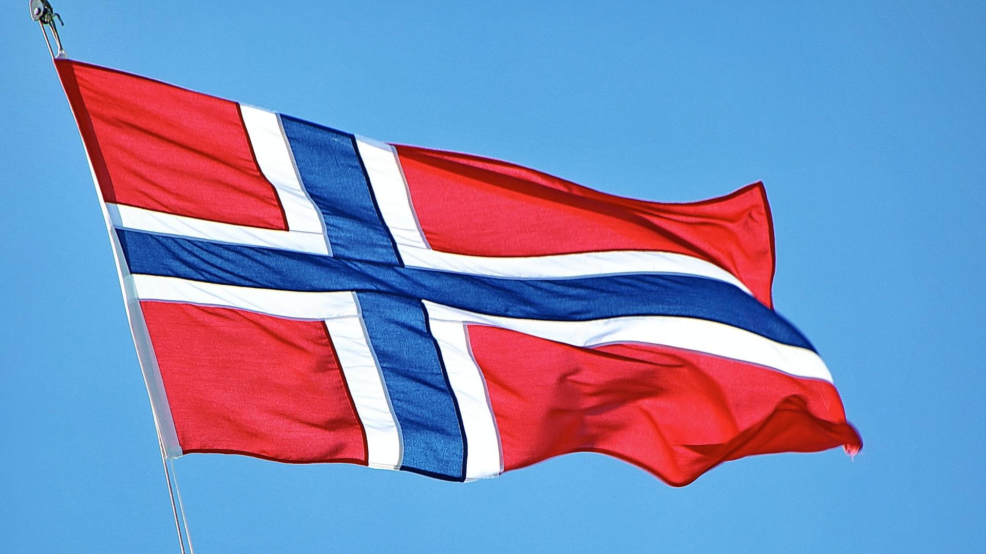 Et norsk flagg som veiver i vinden foran en blå himmel
