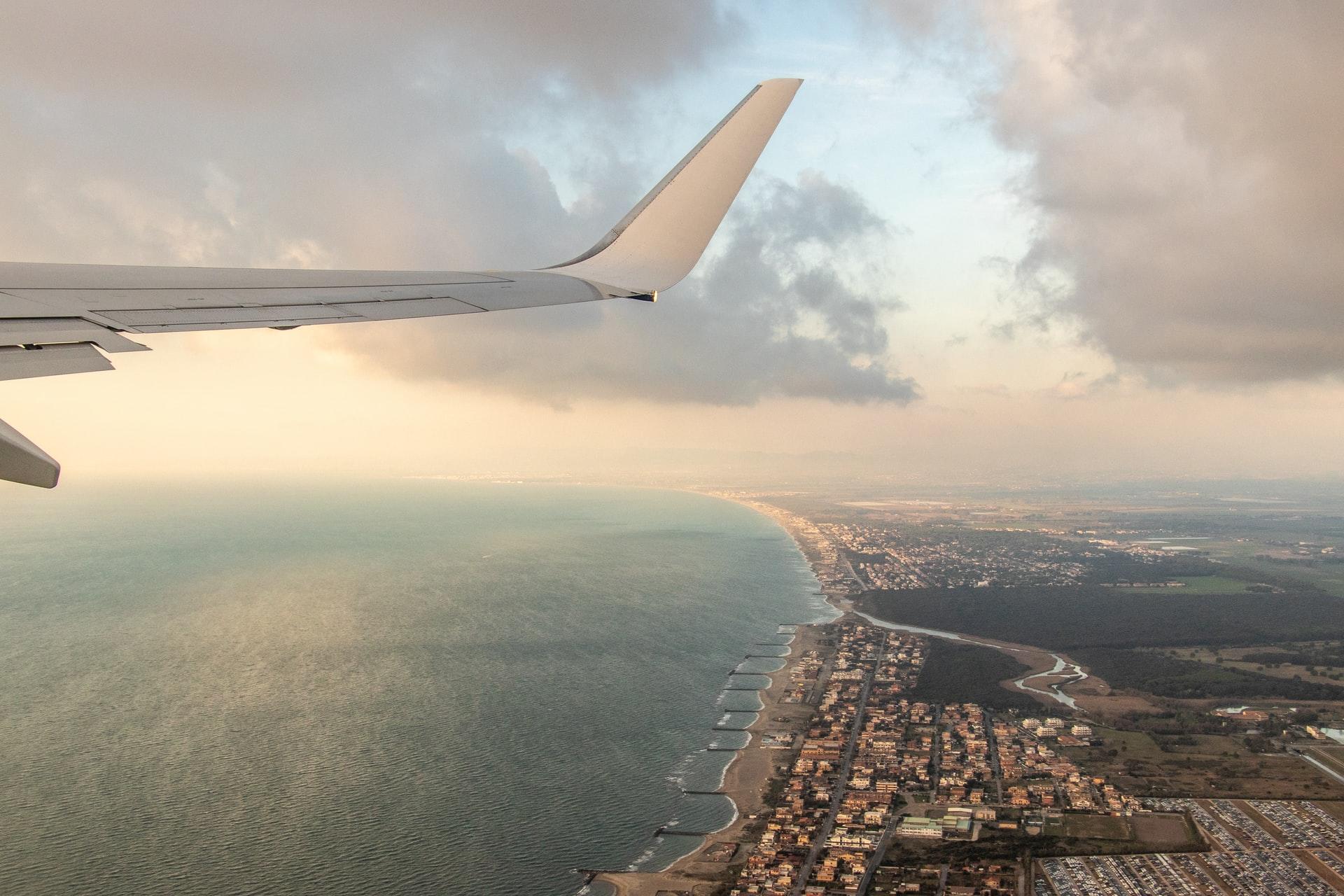 Bilde fra et fly av en flyvinge og utsikt over en italiensk by med kystlinje