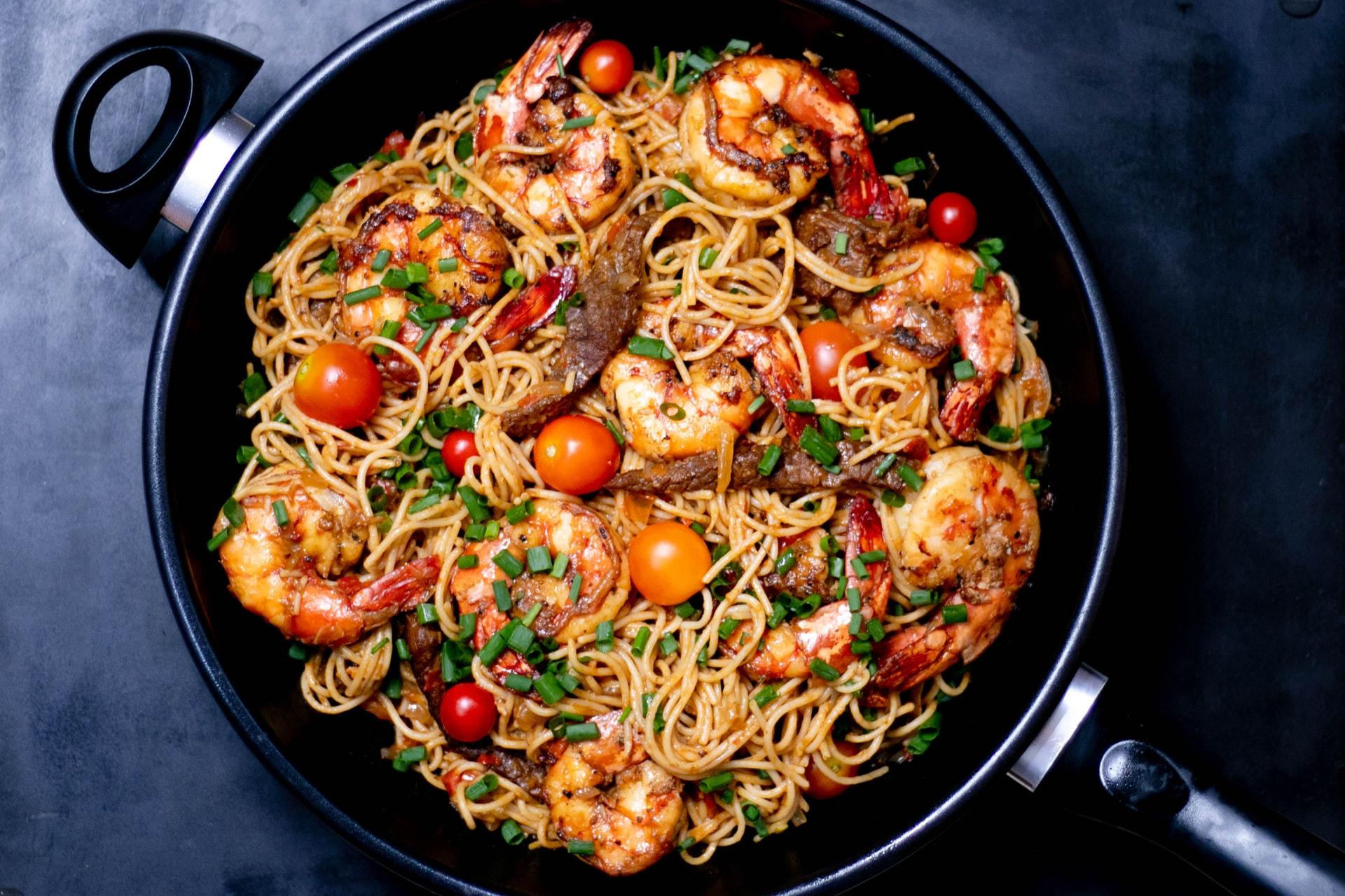 En kjele med en spaghettirett med reker og andre ingredienser