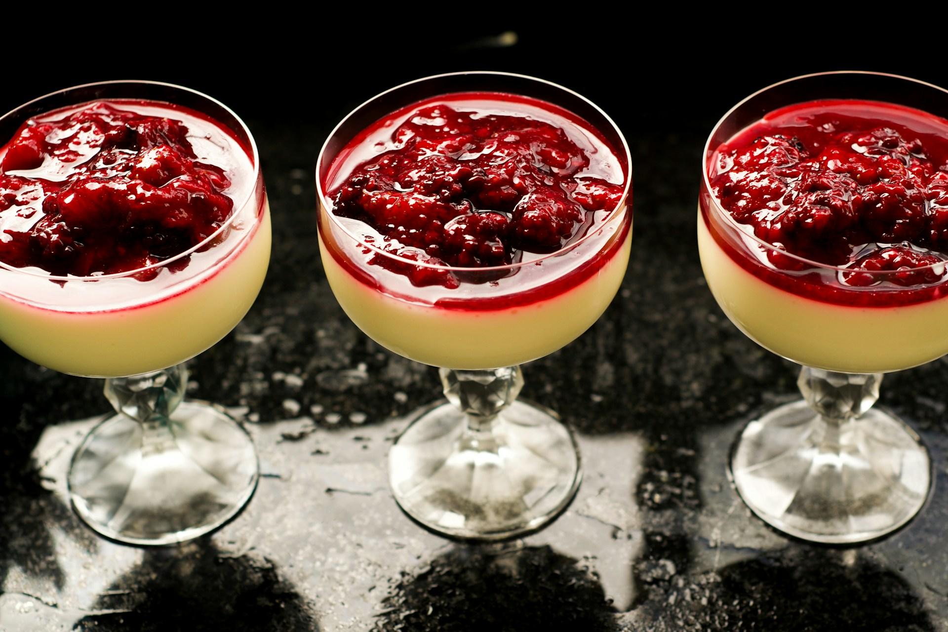 Tre glass med stem fylt med panna cotta og bær på toppen.