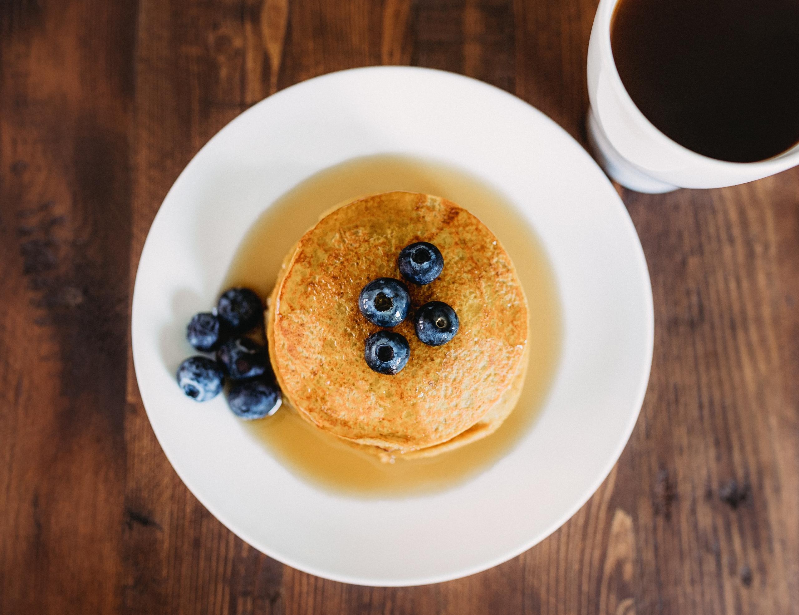 amerikanske pannekaker med blåbær fotografert ovenfra, ved siden av en kopp med det som på tysk heter Kaffee