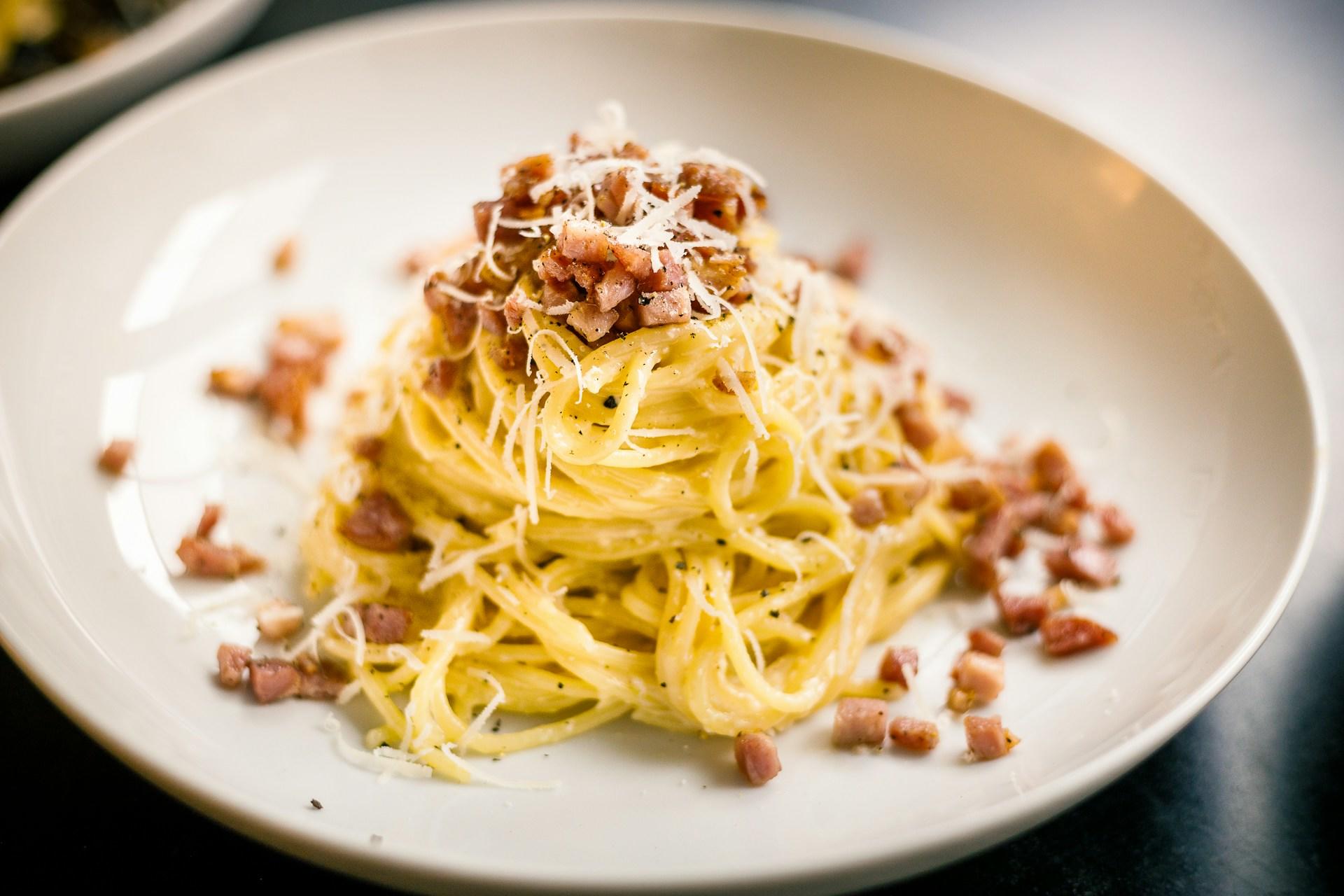 Hvit tallerken med pent dandert spaghetti carbonara med bacon.
