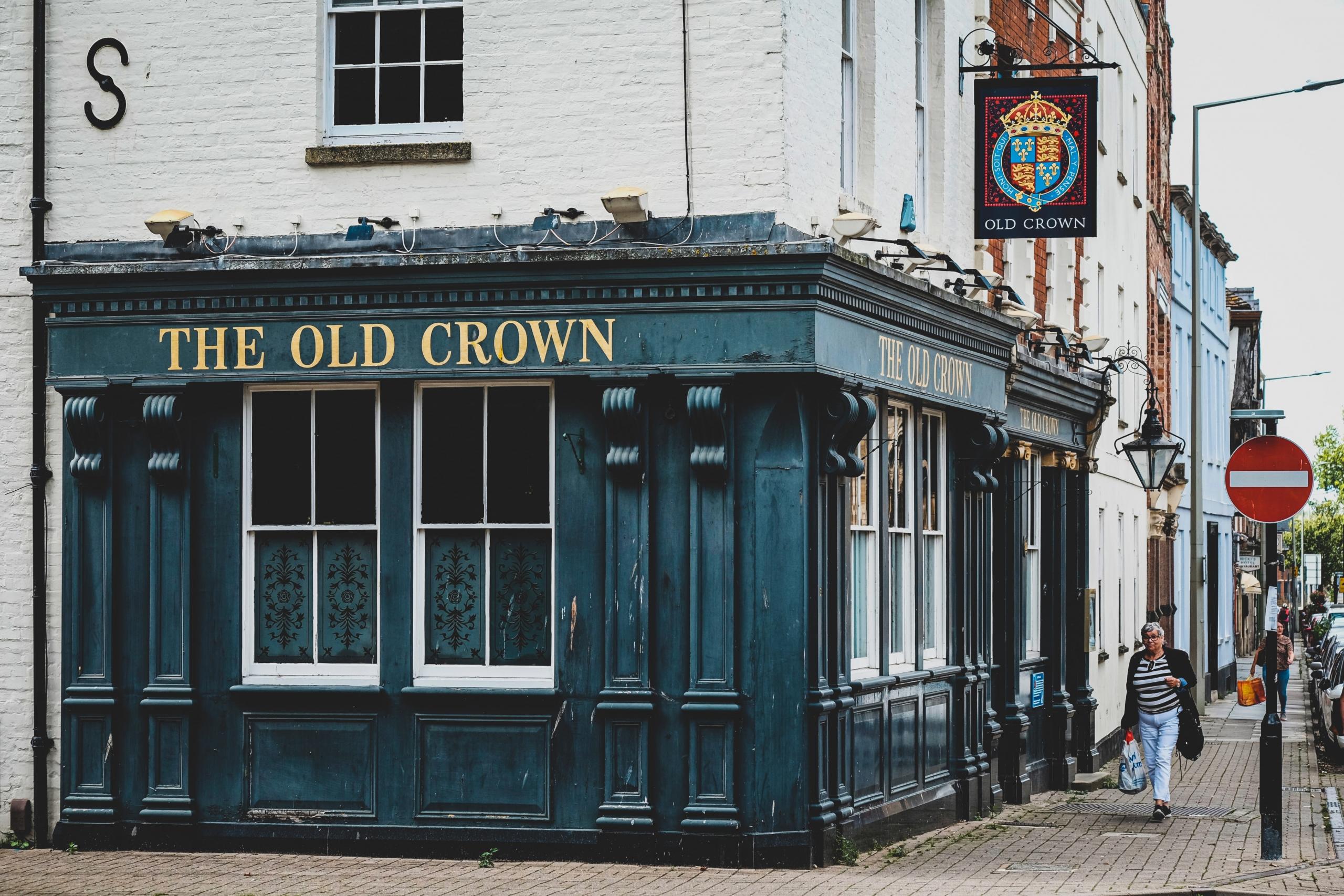 en pub ligger på hjørnet av en hvit murbygning, det står "the old crown" over vinduene