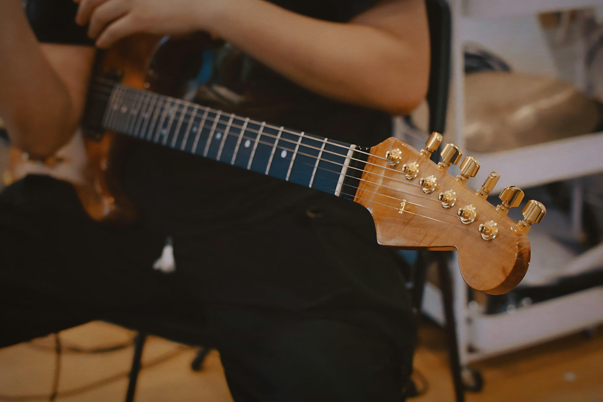Man som sitter på en stol med gitar på fanget.