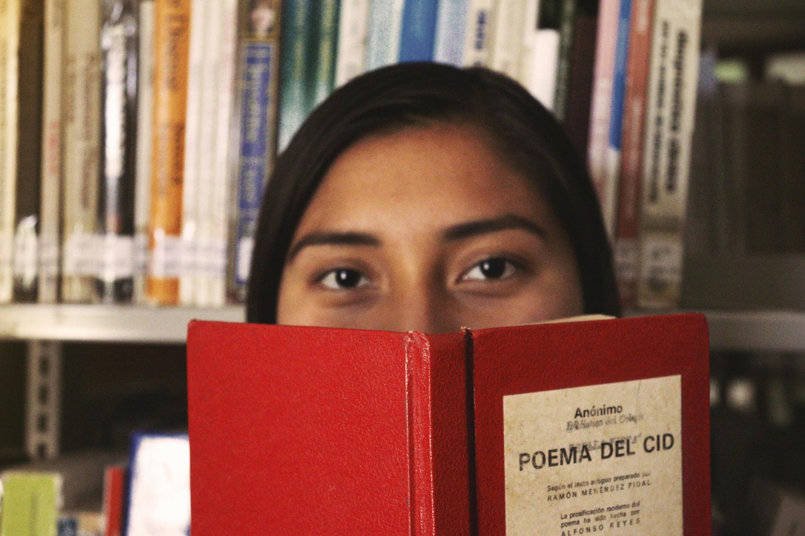 ung kvinne holder en rød bok med tittelen "poema del cid", hun skal lese den på spansk
