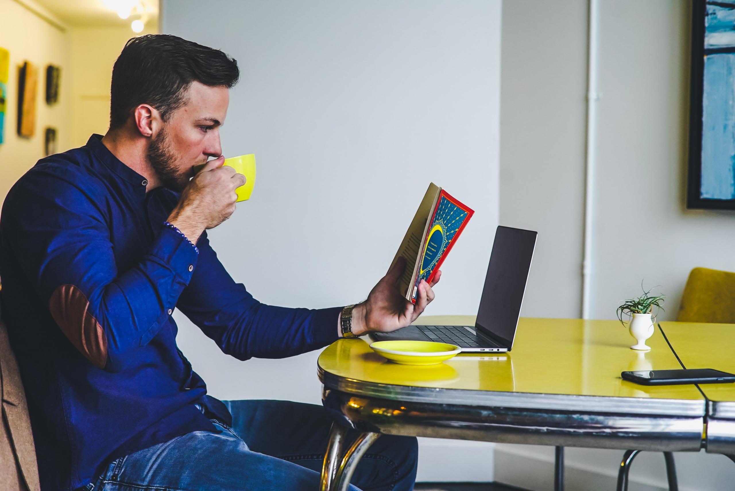 en mann leser en spansk bok mens han sitter foran en laptop