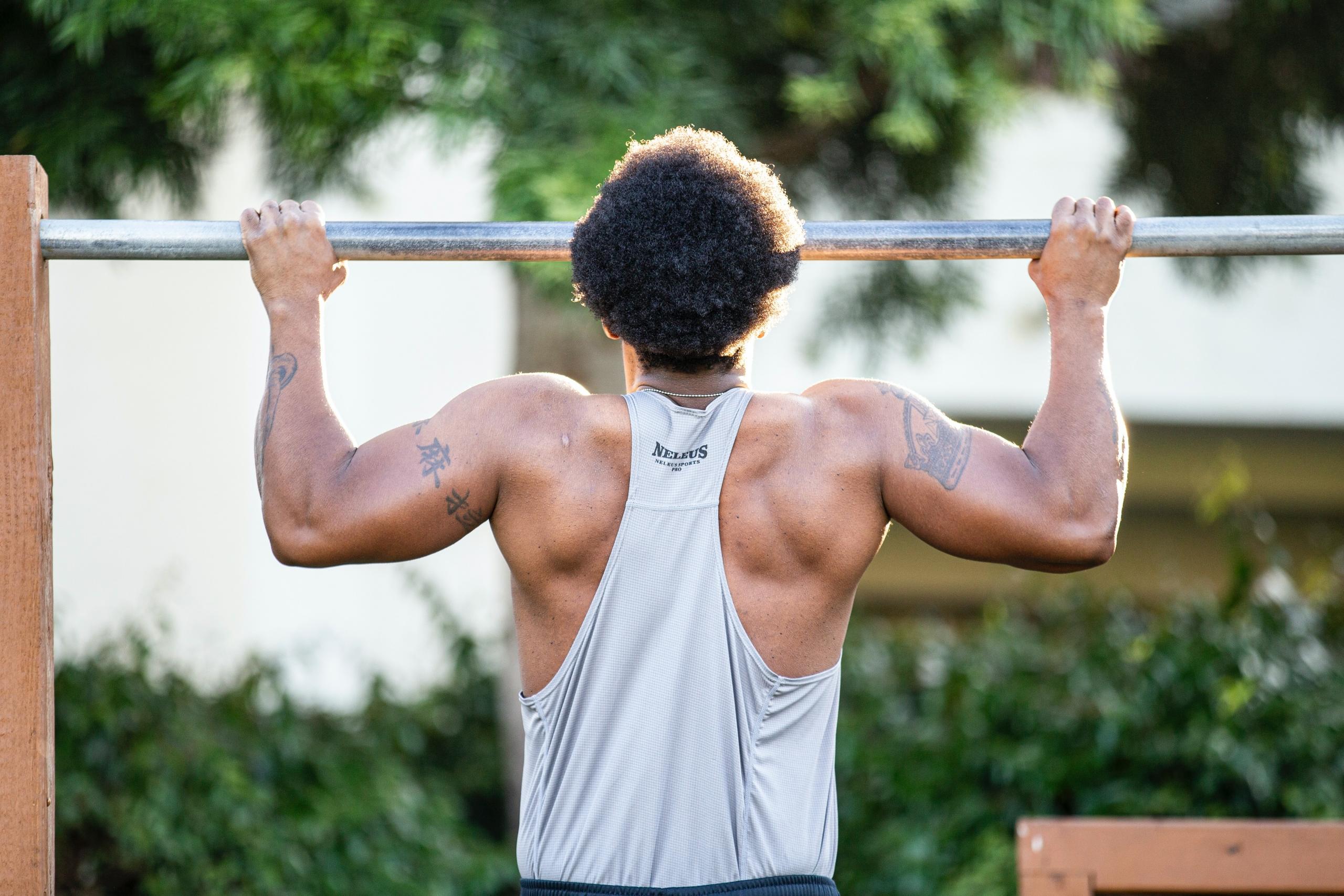 mann tar pull ups for å trene armstyrke på en utendørs treningsplass