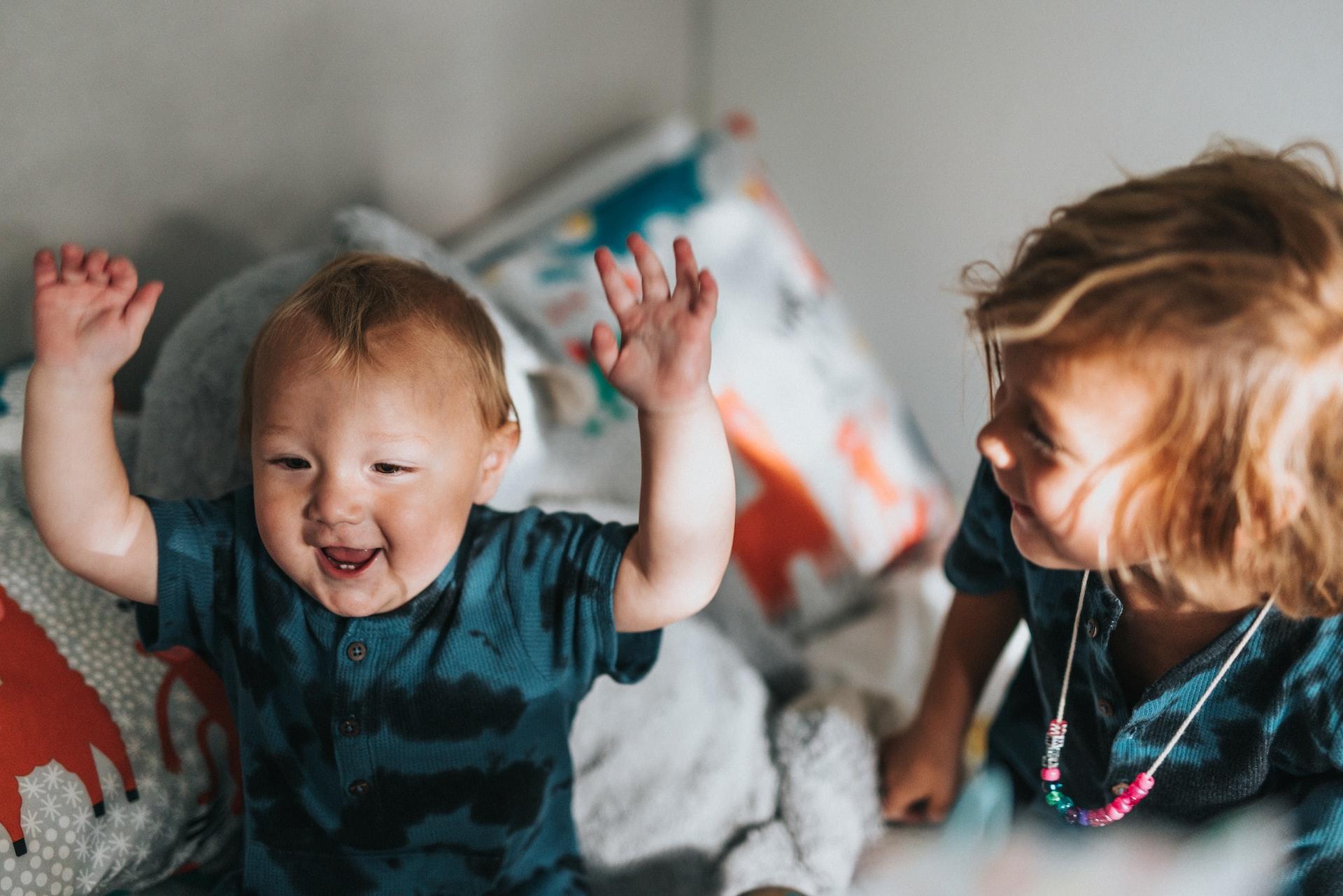 Liten gutt sitter sammen med en litt eldre jente, og har armene opp i været og smiler bredt.