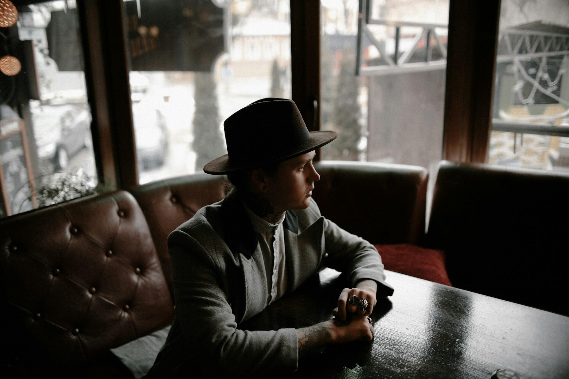 Mystisk mann med hatt sitter alene på en kafé