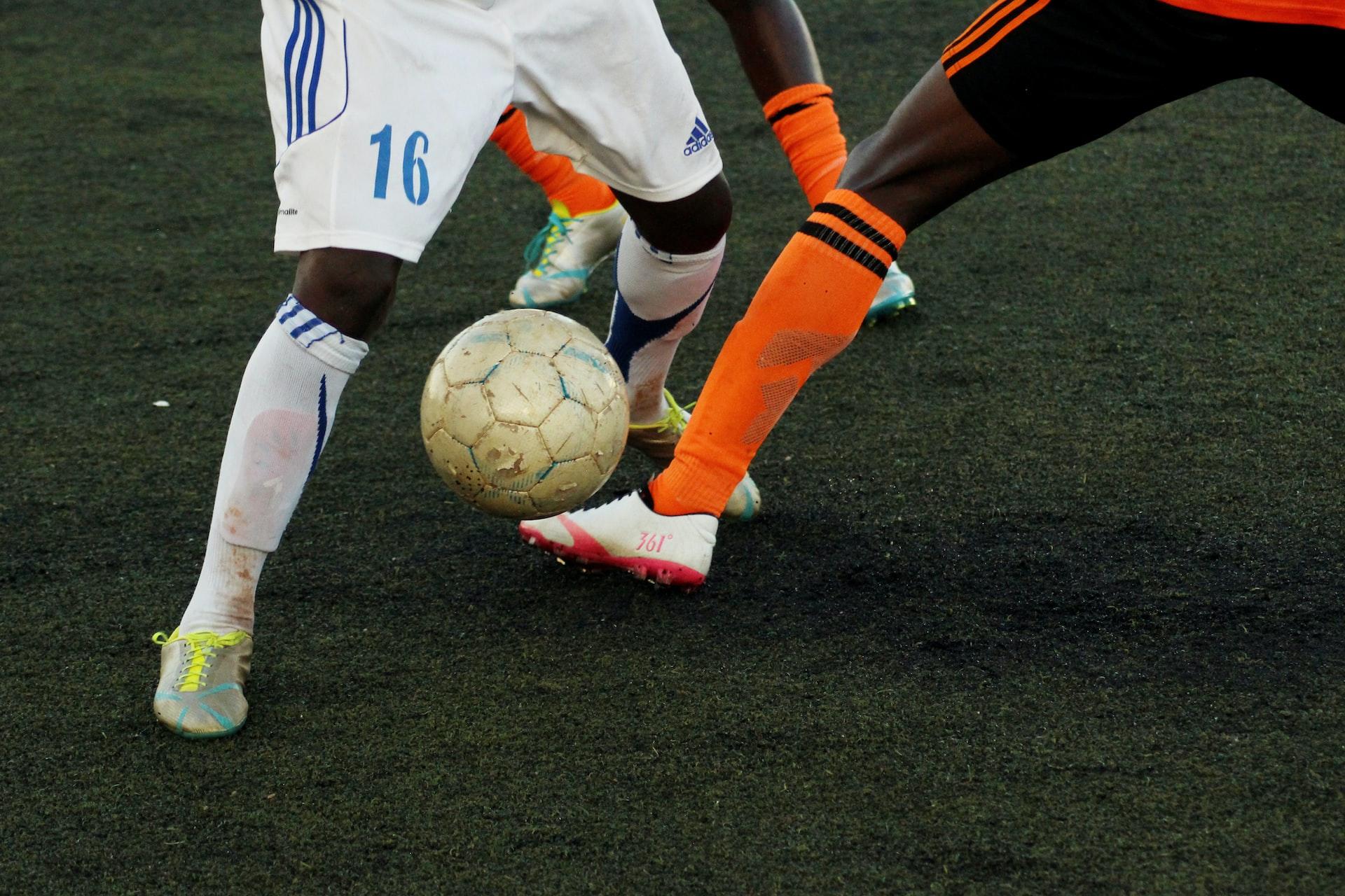 Mann med hvit fotballdrakt spiller mot mann med oransje fotballdrakt.