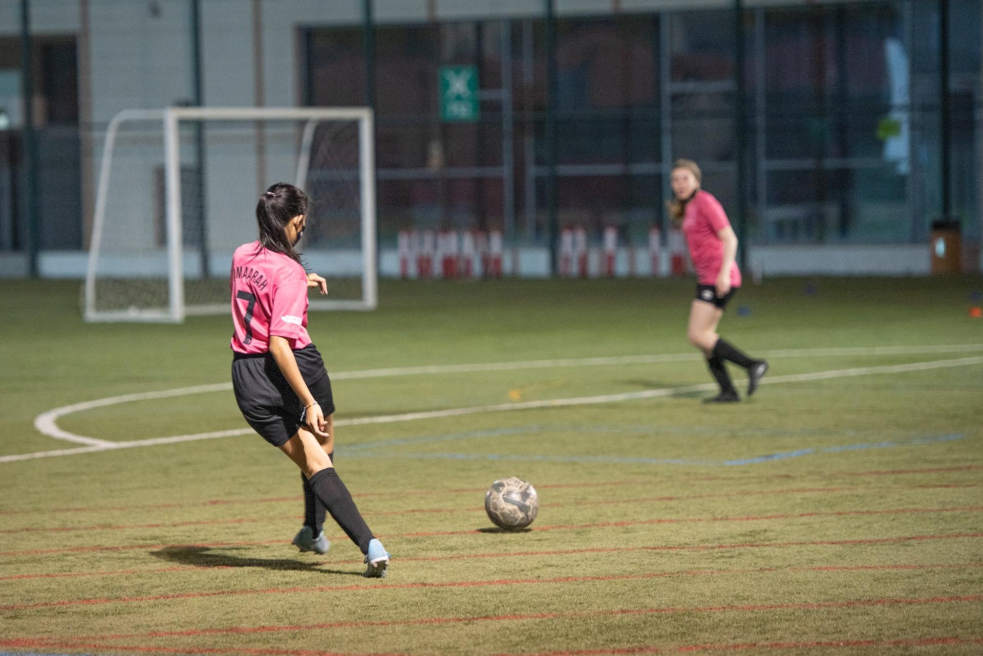 Jente med langt mørkt hår og rosa drakt skal til å skyte på på mål i en fotballkamp.